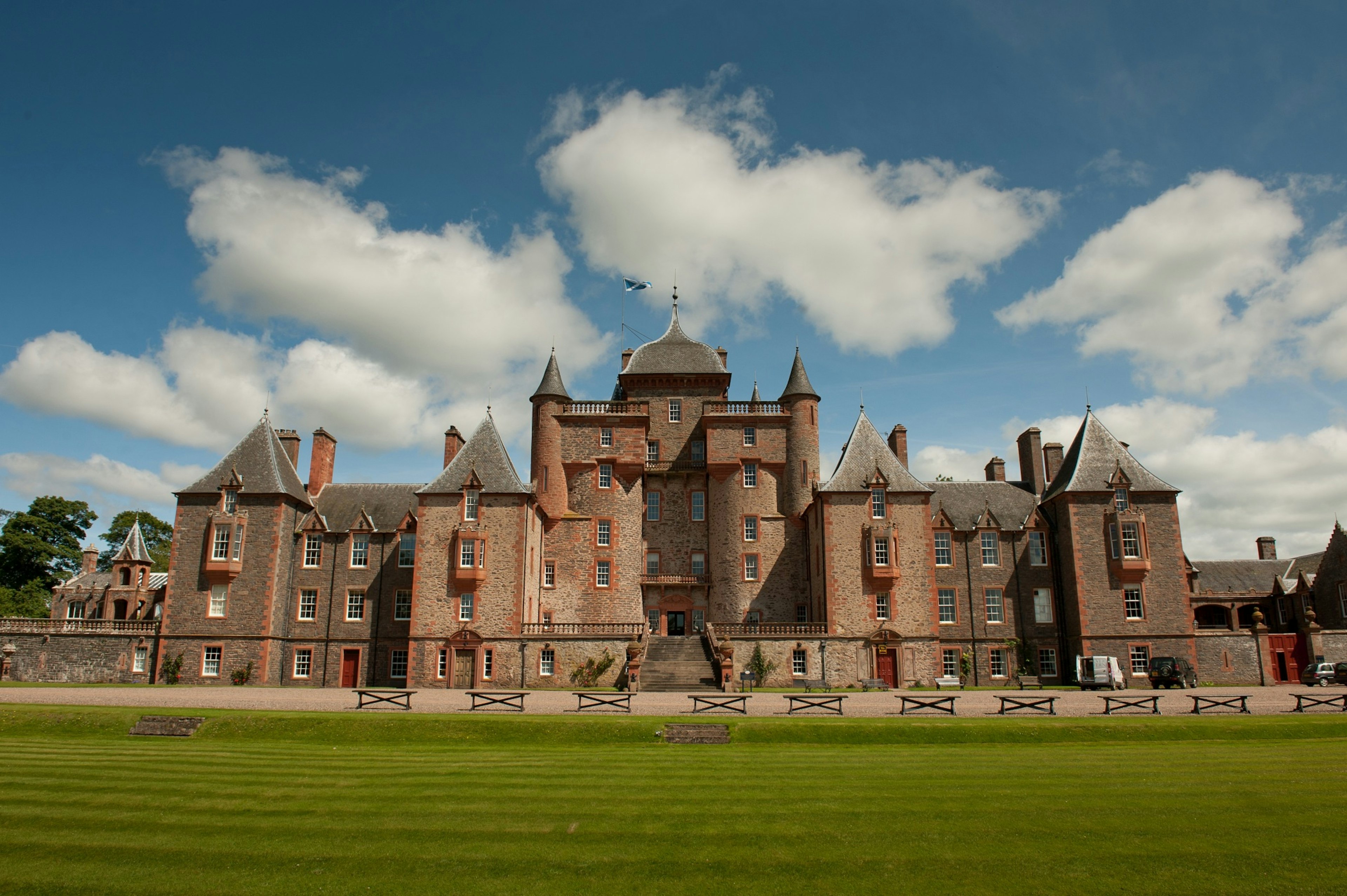 A vast red-brick 16th-century castle flying a Scottish flag stands behind a manicured lawn