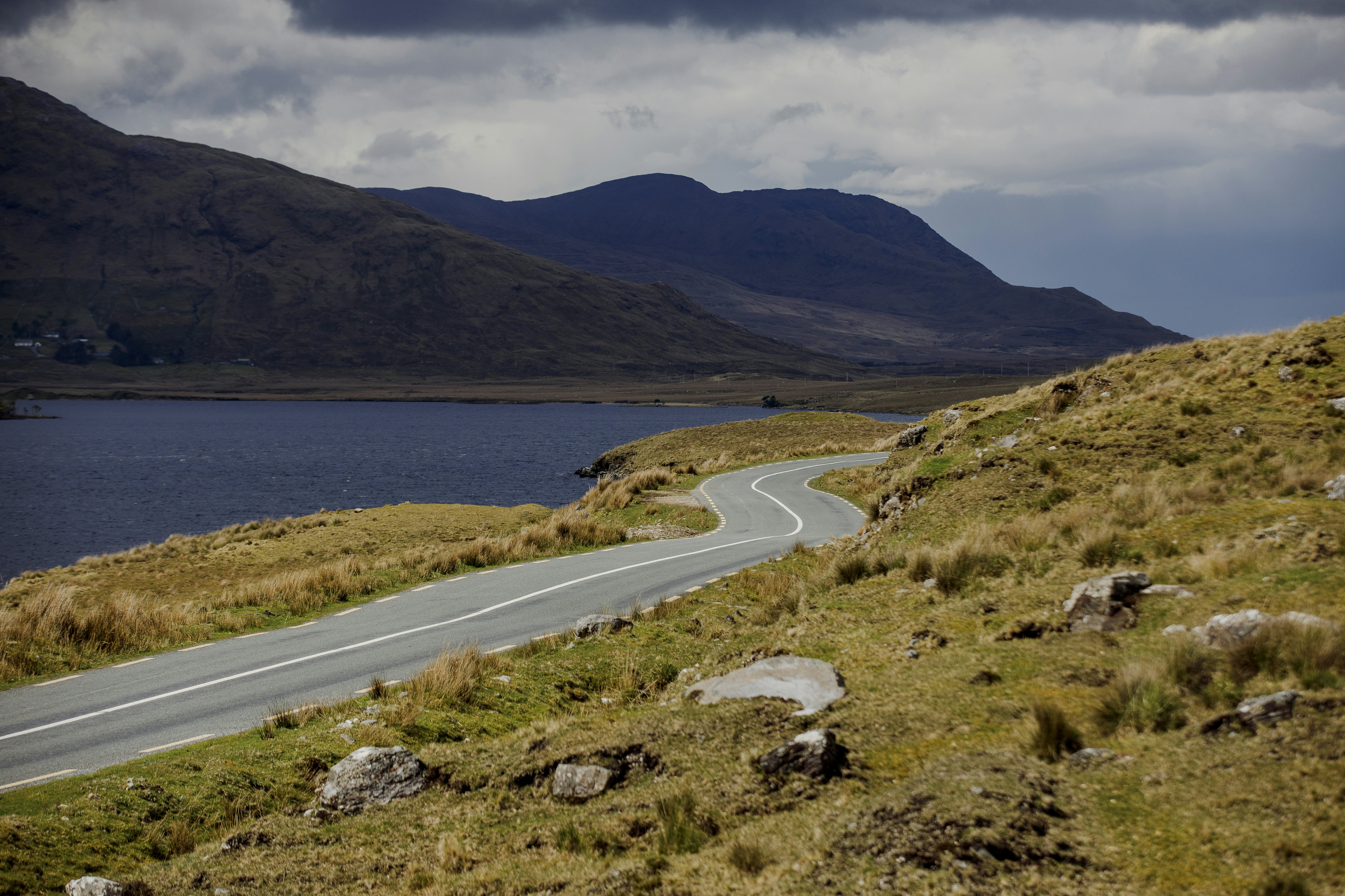 A road runs along the edge of a lake, with green hills rolling in the background.