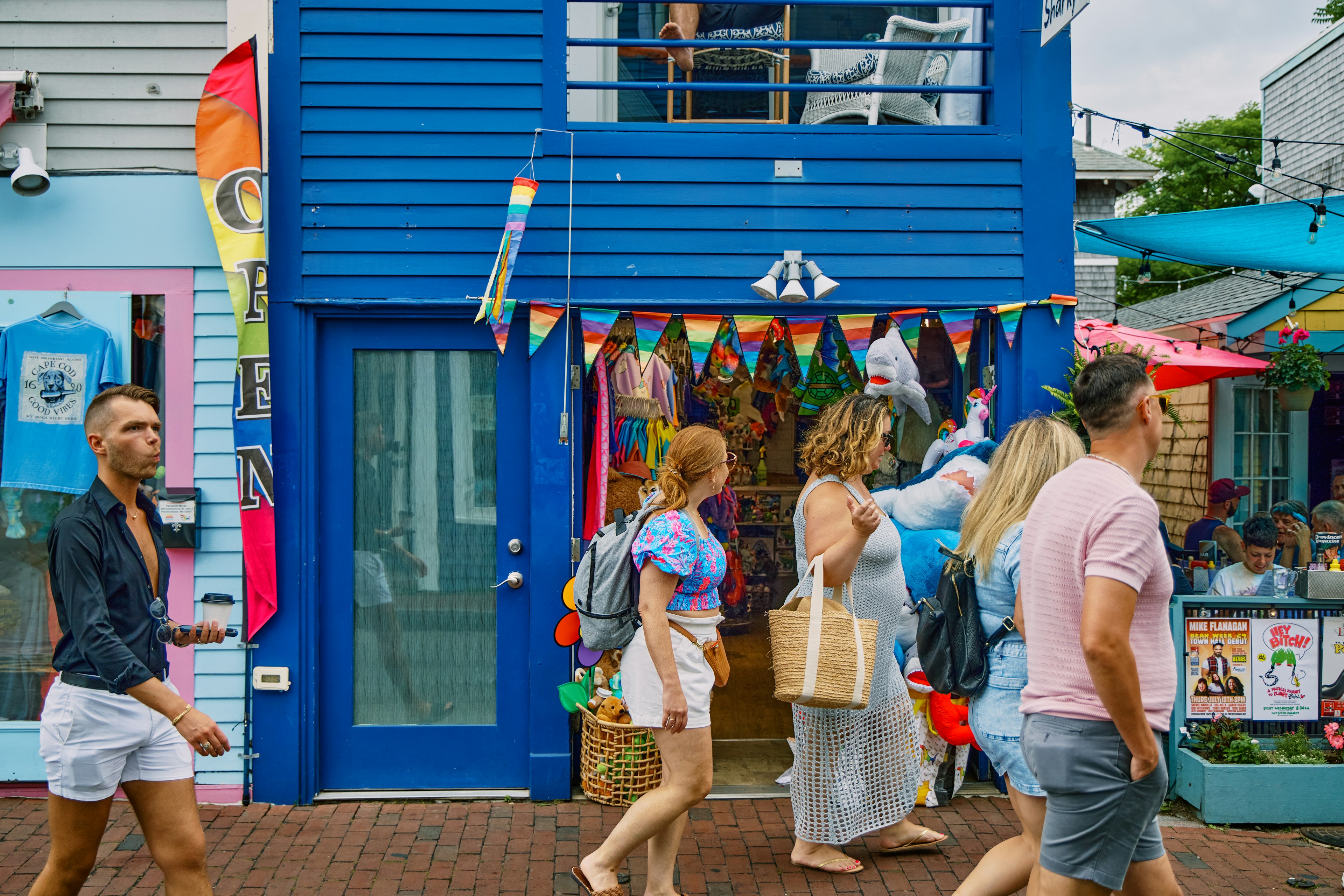 People on a brick sidewalk past a storefront painted blue and festooned in rainbow flags