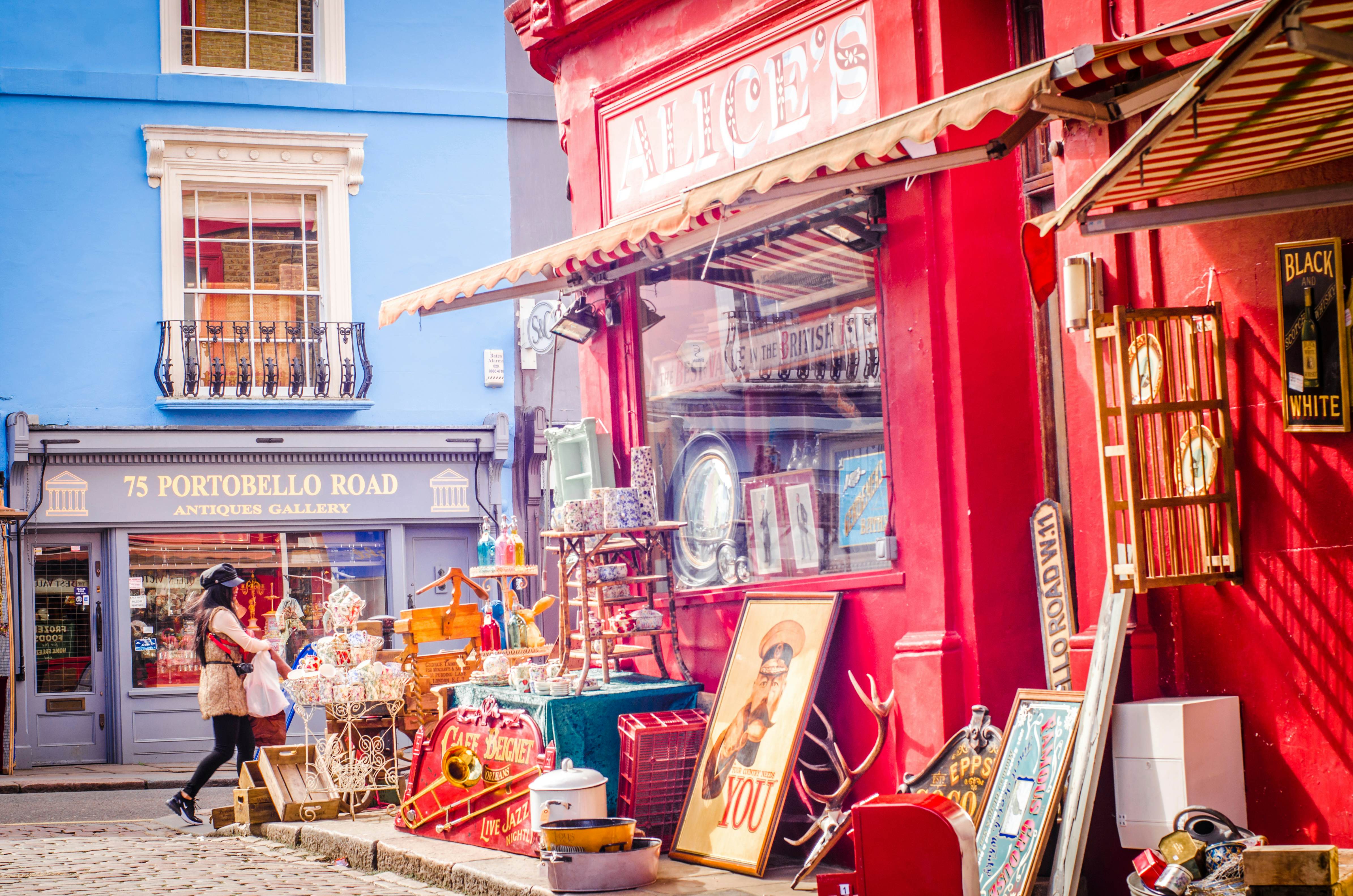 Shoppers walking past antique shops on a street with antiques on display and shopfronts in pastel colors