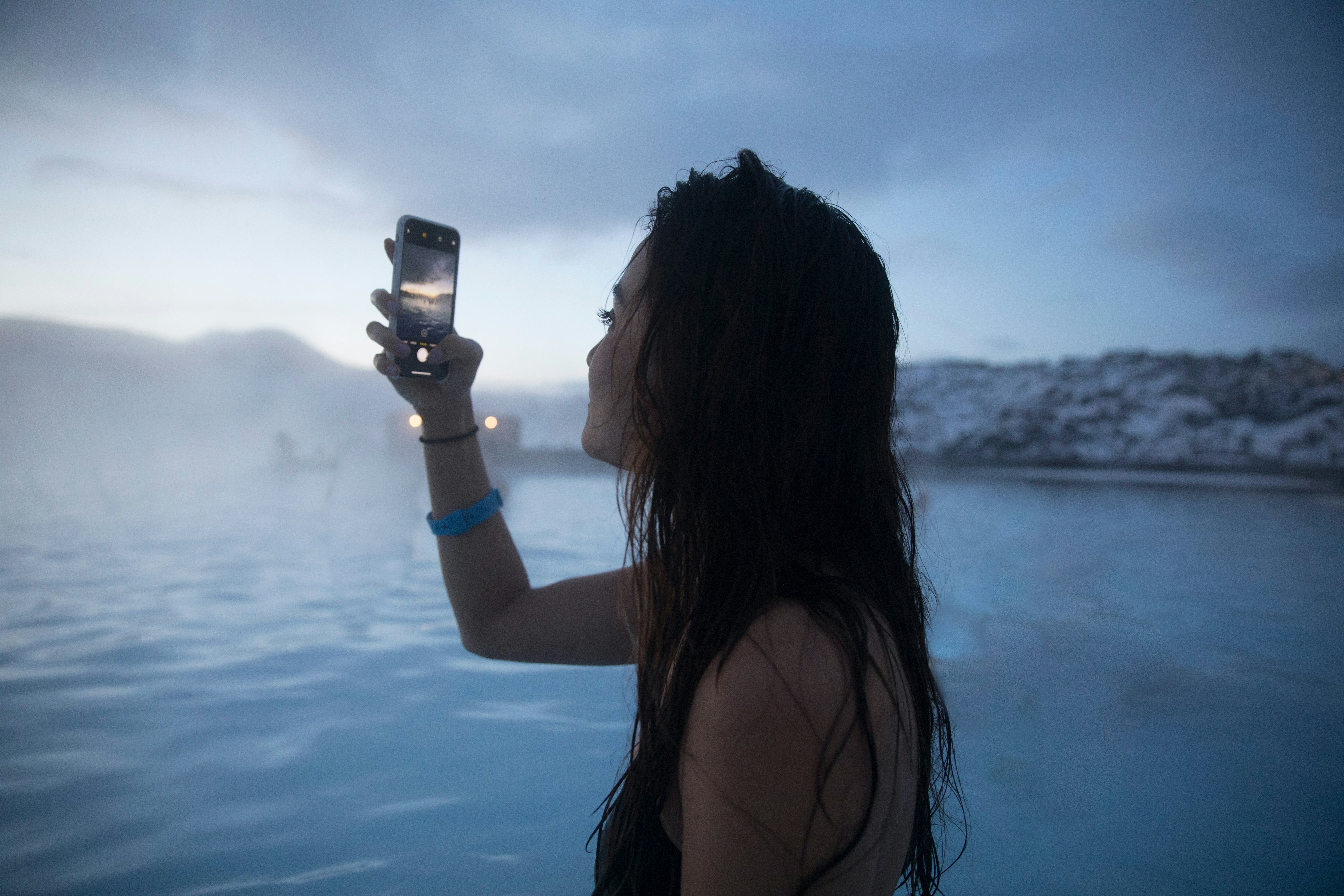 A young female tourist holds her phone to take a photo in the pool of the Blue Lagoon Geothermal Spa in Iceland