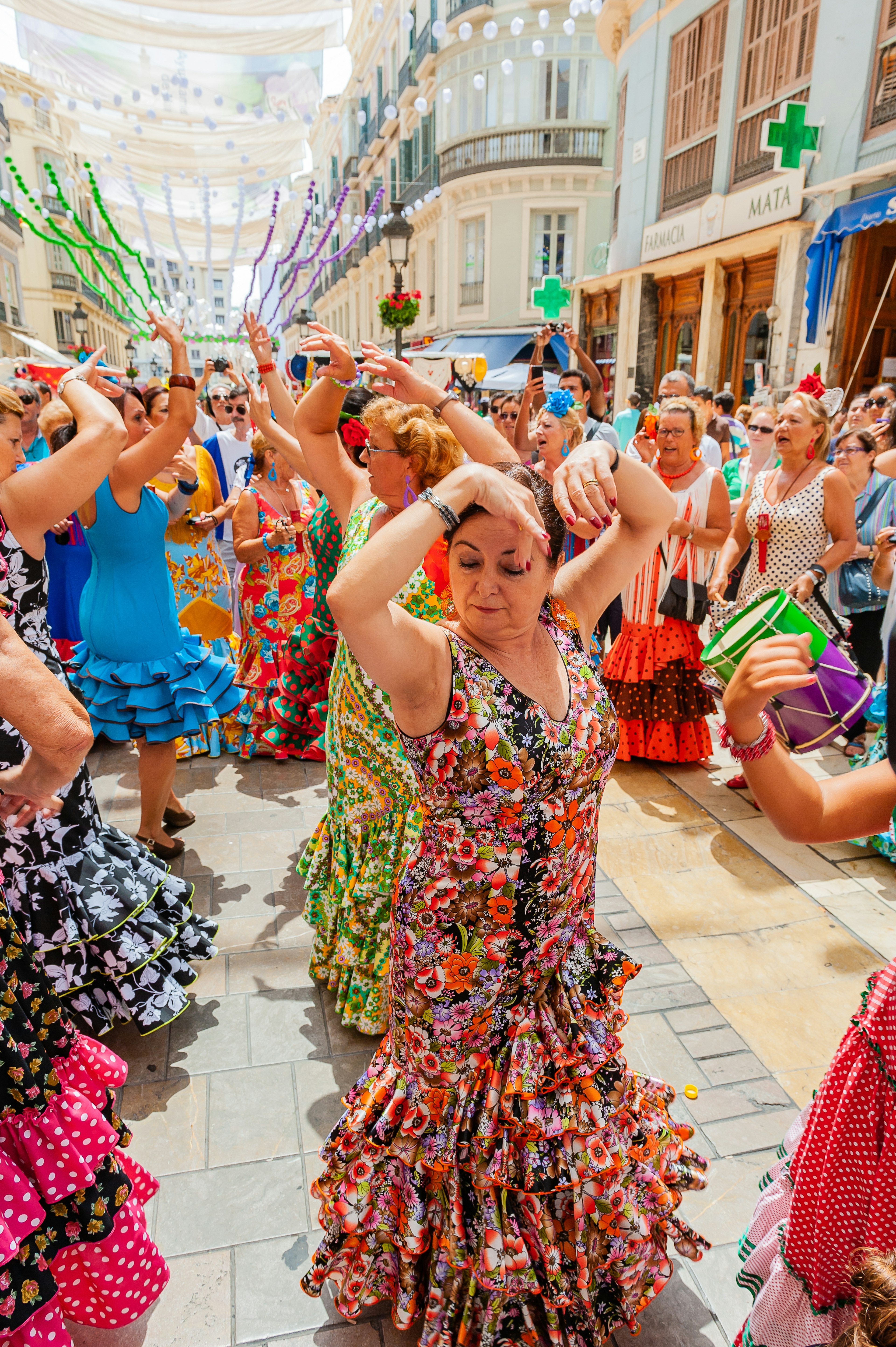 Many flamenco dancers in colorful dresses perform for a crowd in the streets of Malaga during the mid-August celebration of Feria de Málaga.