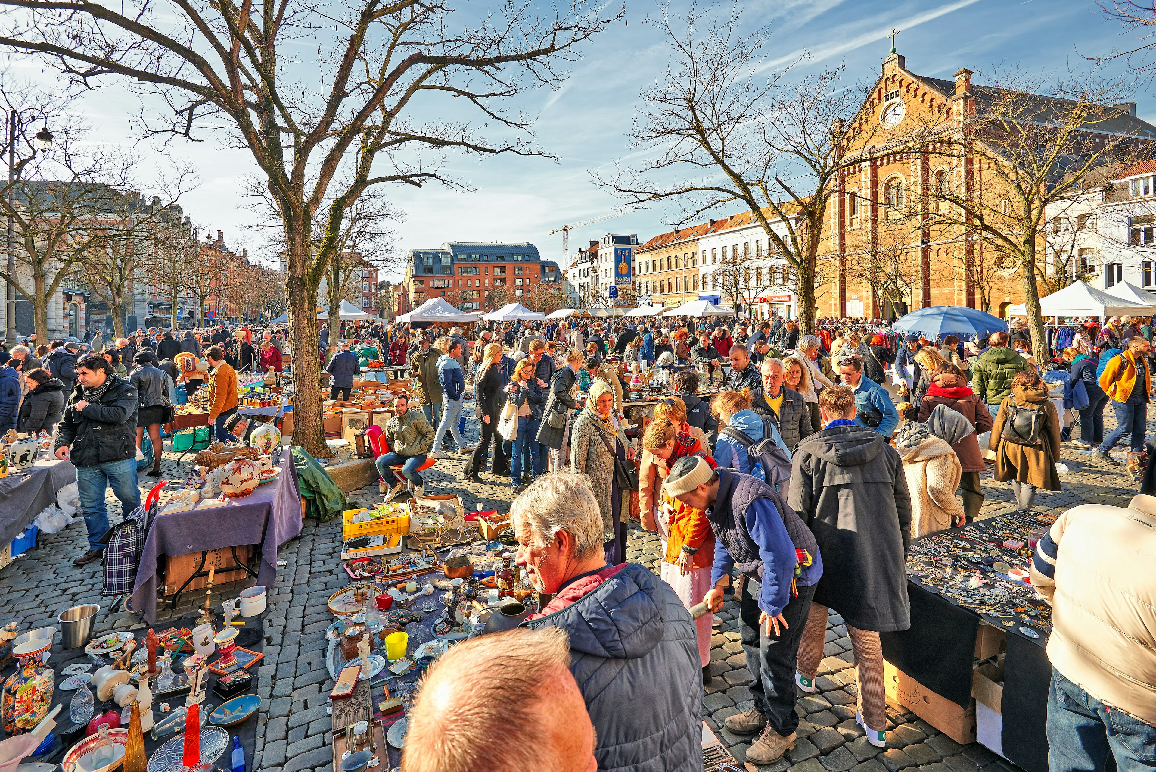 Tables in a cobbled square stacked high with crockery, trinkets and ornaments, with shoppers browsing the market