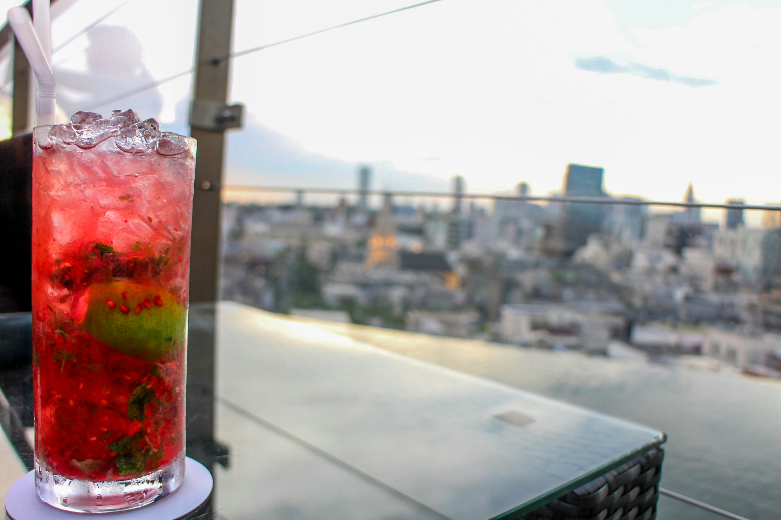 A red cocktail on a table in a rooftop bar with the Tokyo skyline stretching out as the sun sets