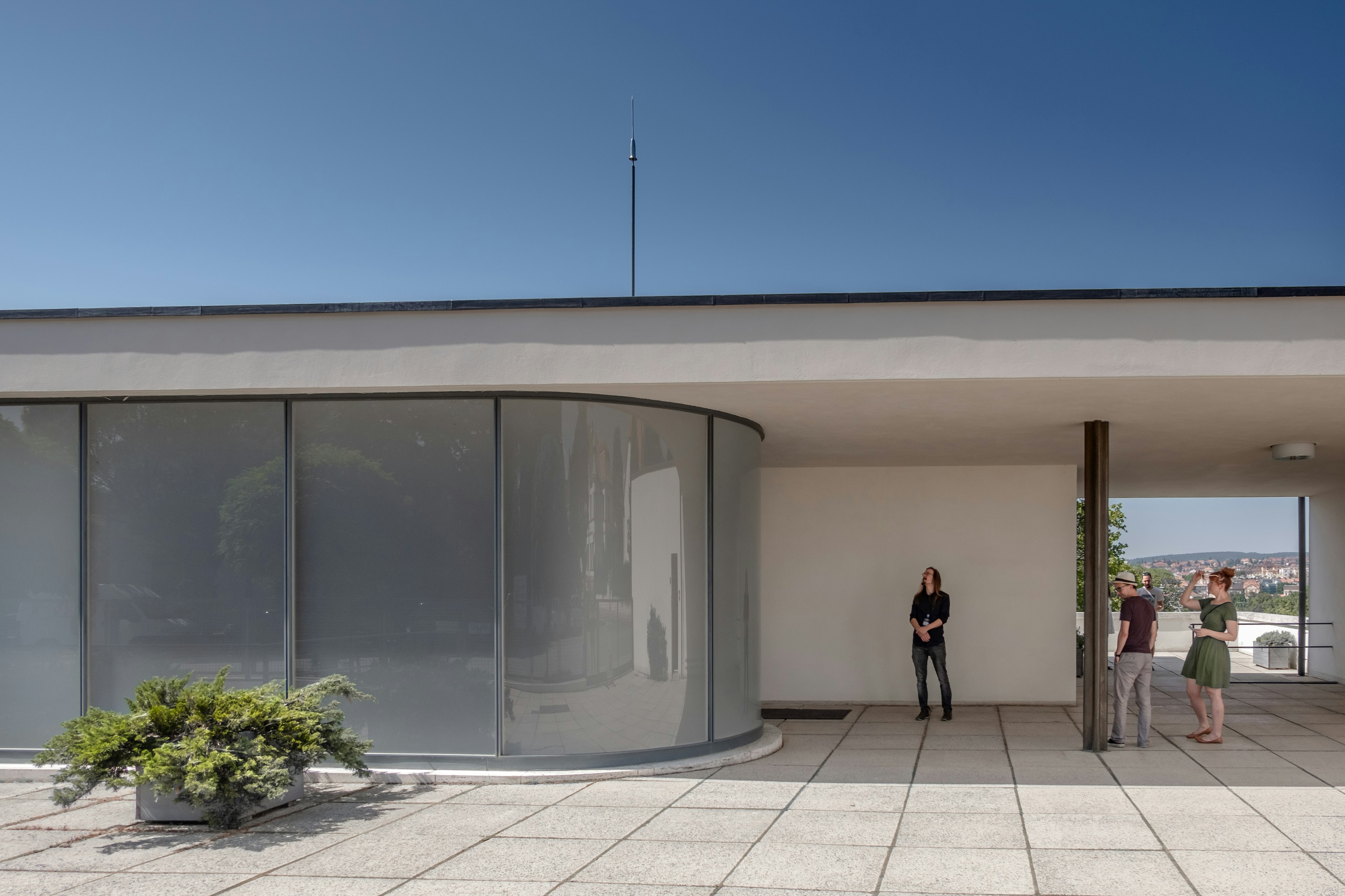 Women stand on the terrace of a modern villa next to a curved, floor-to-ceiling glass window