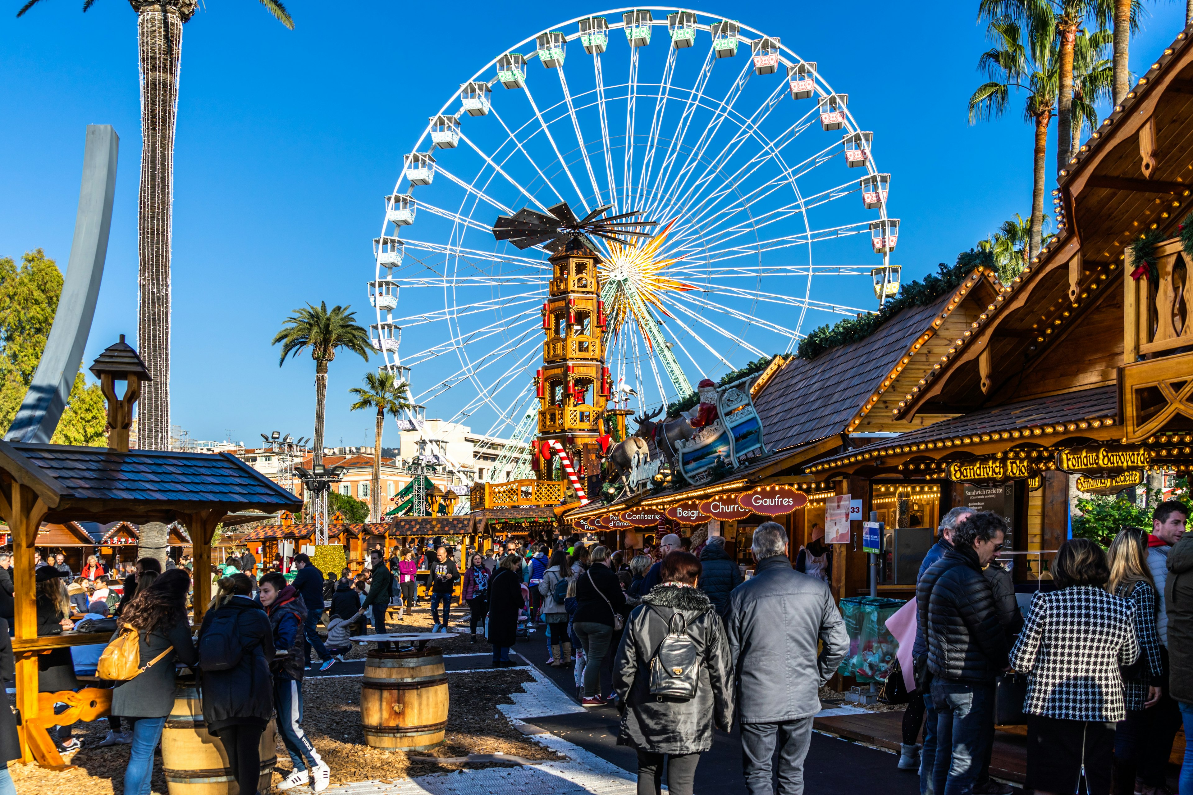 People shopping between the stalls of Nice Christmas market under the Ferris wheel