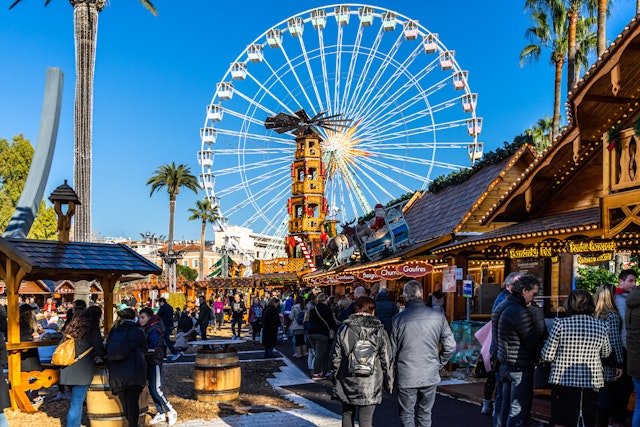 People shopping between the stalls of Nice Christmas market under the Ferris wheel