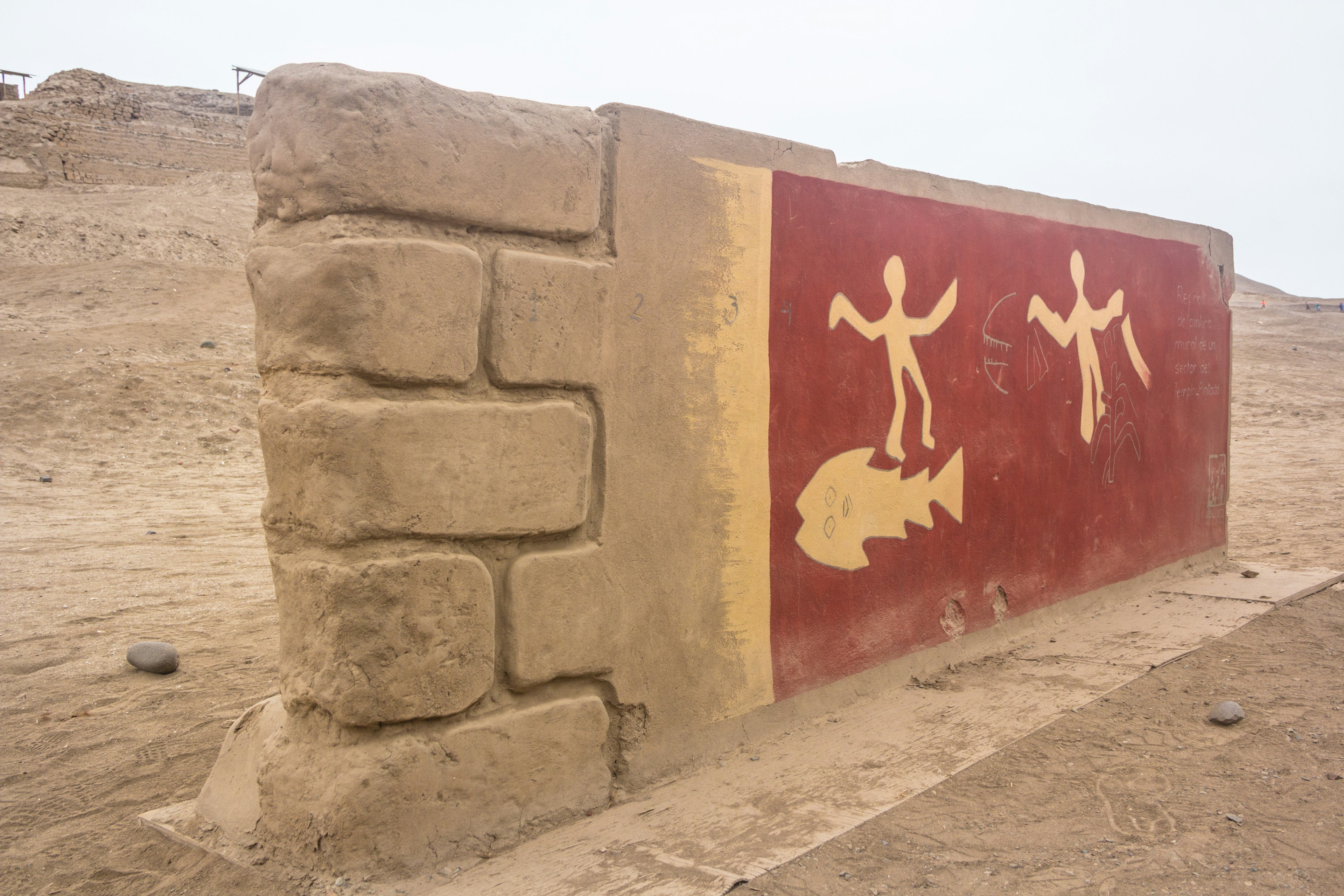 A reconstructed fragment of an ancient wall and petroglyphs depicting figures and a fish in the desert