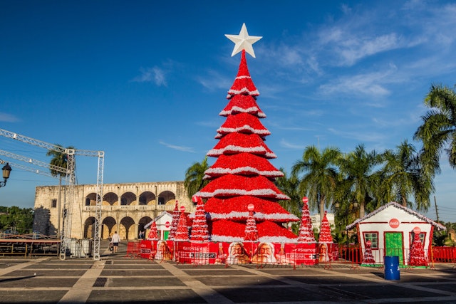 A red Christmas tree stands by palm trees and the historic Alcazar de Colón, Santo Domingo, Dominican Republic