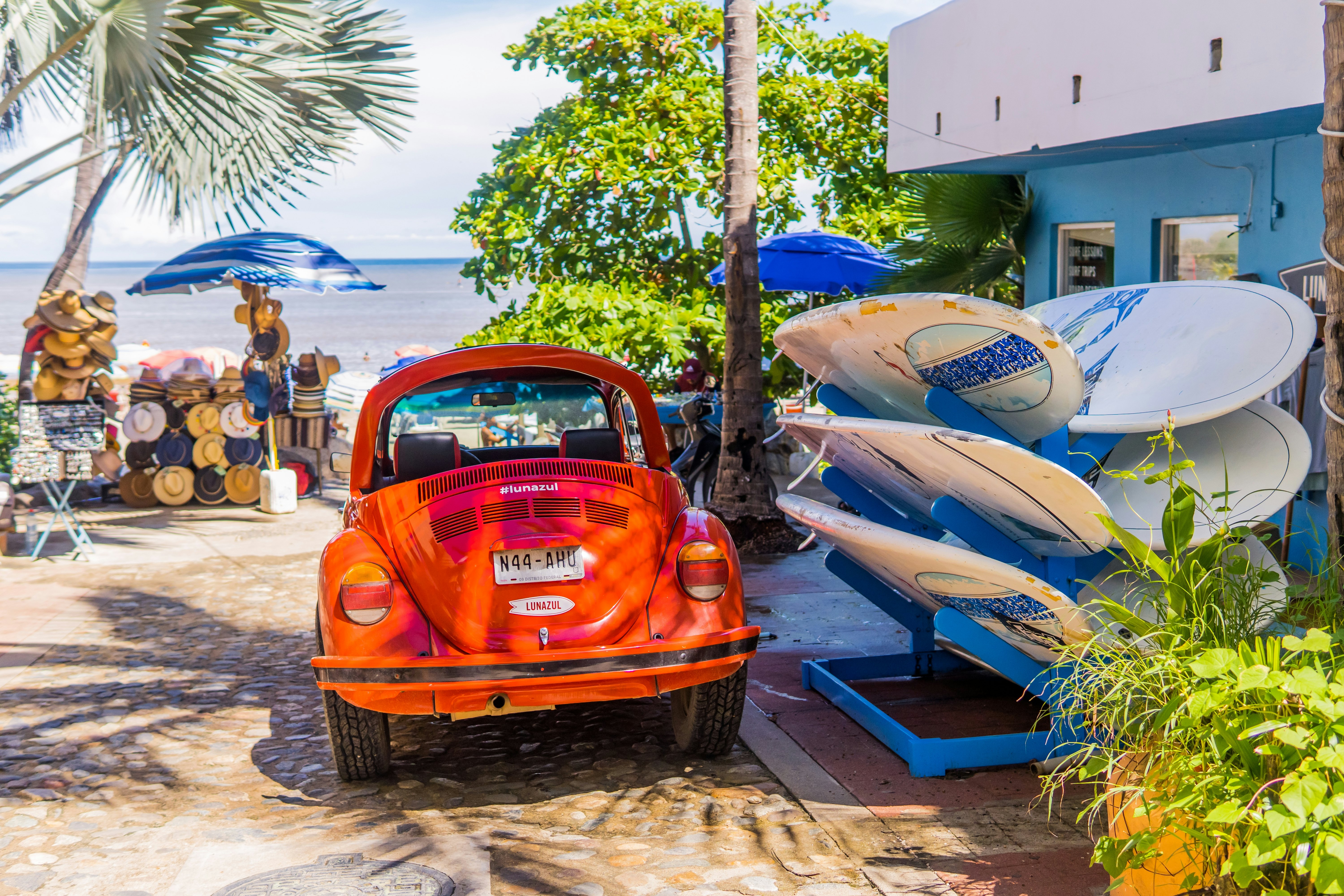 A classic red VW Beetle (vocho) is parked next to surfboards a few feet from the beach