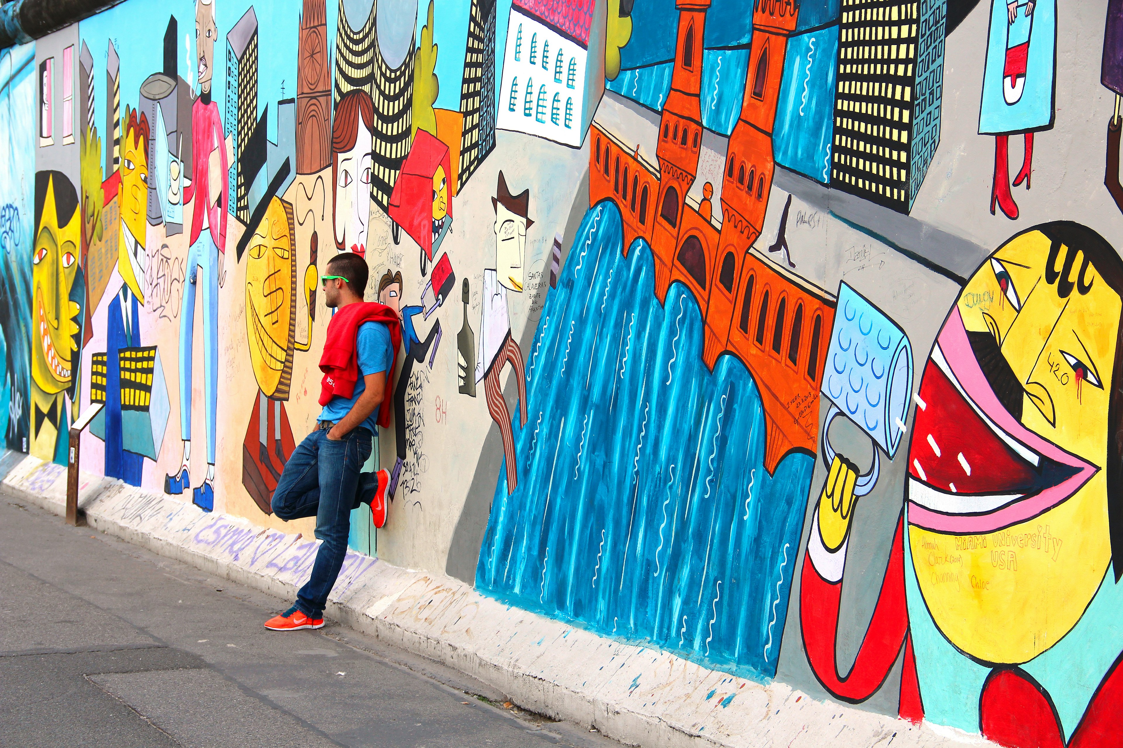 A man leans on a wall covered in large colorful murals of smiling faces