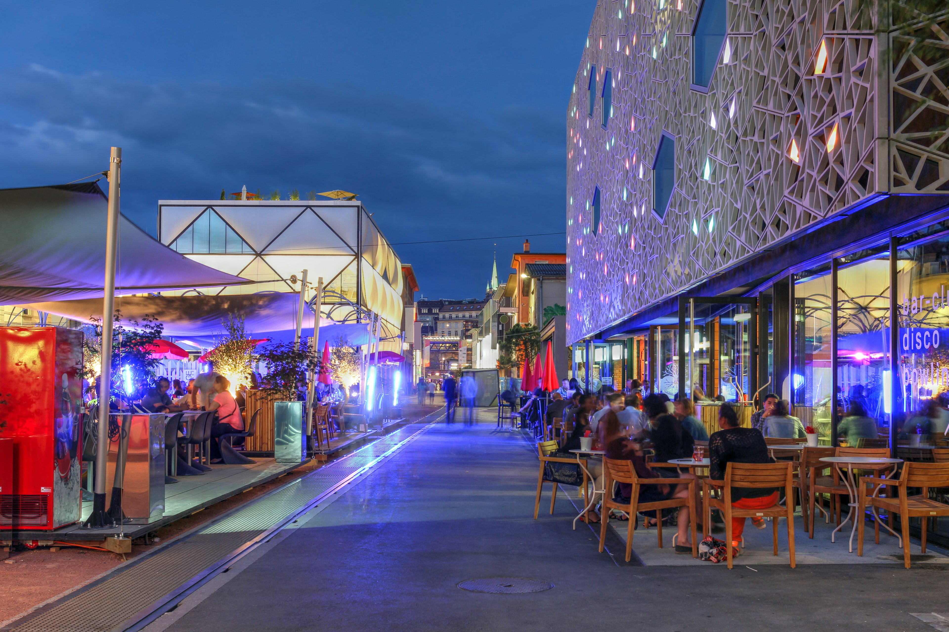 Night scene in a city with people sat outside cafes and bars in a modern district