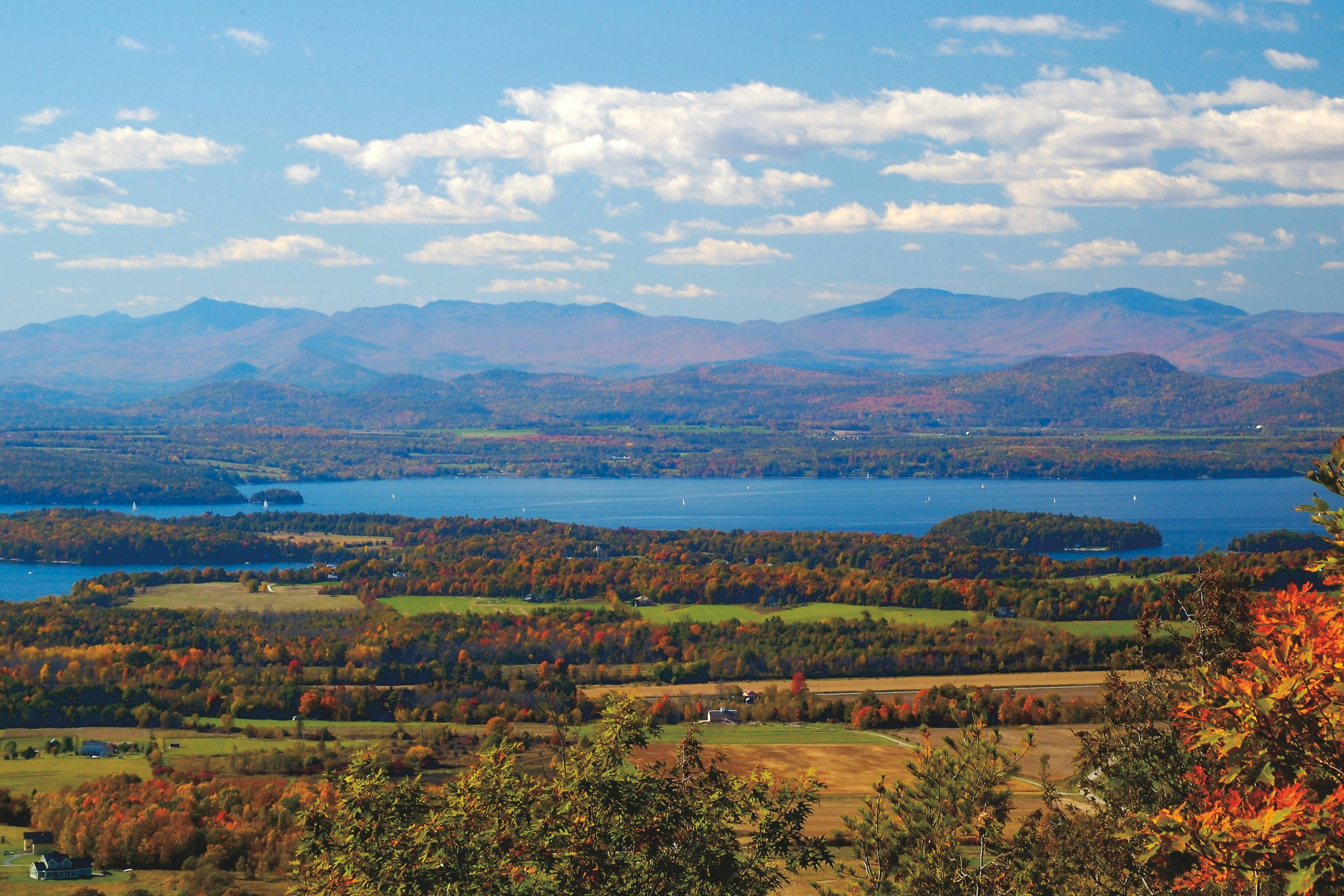 Fall colors in the trees and woodland surrounding a large lake and distant mountains