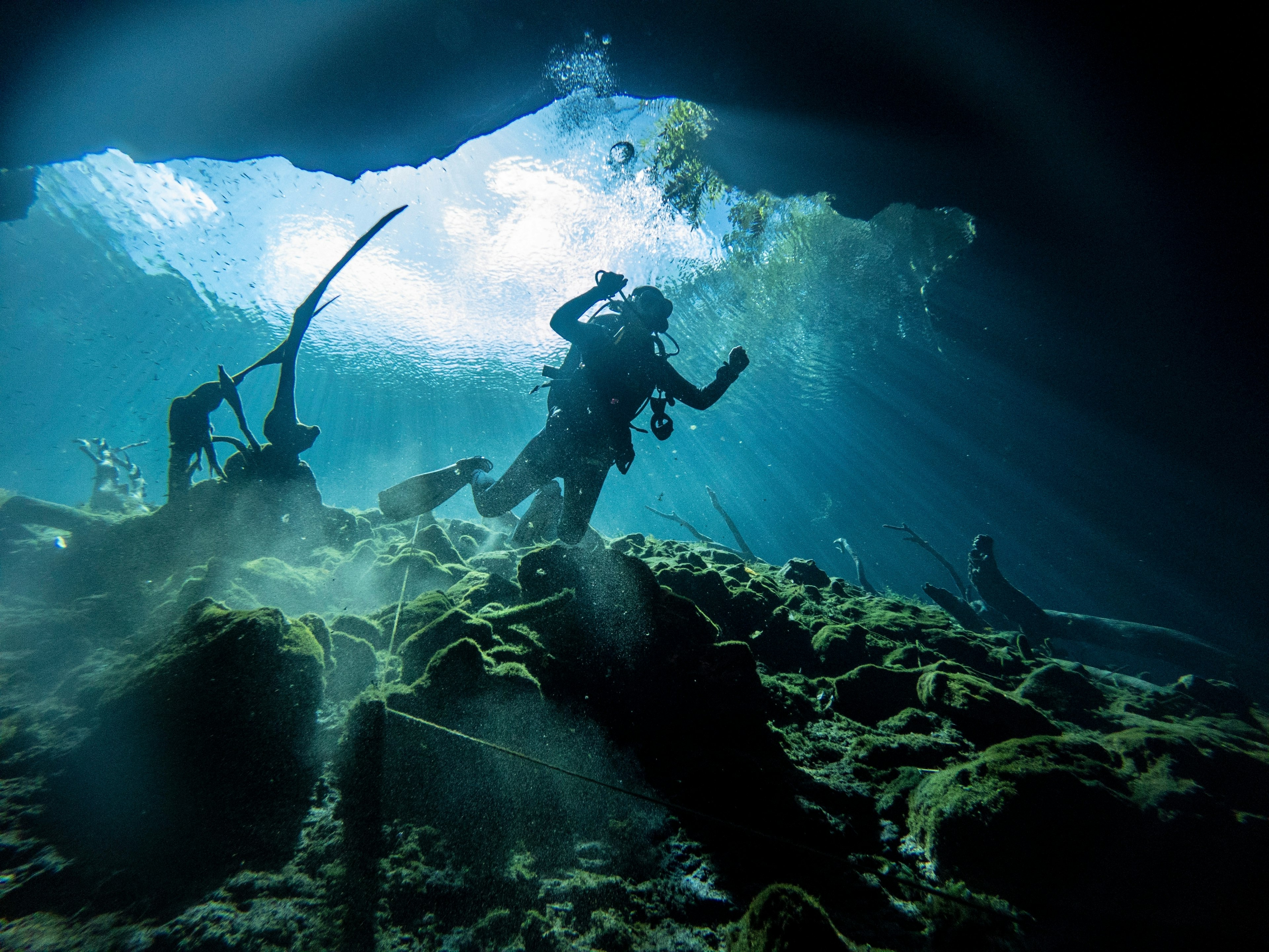 A scuba diver in silhouette as light fills a flooded cave