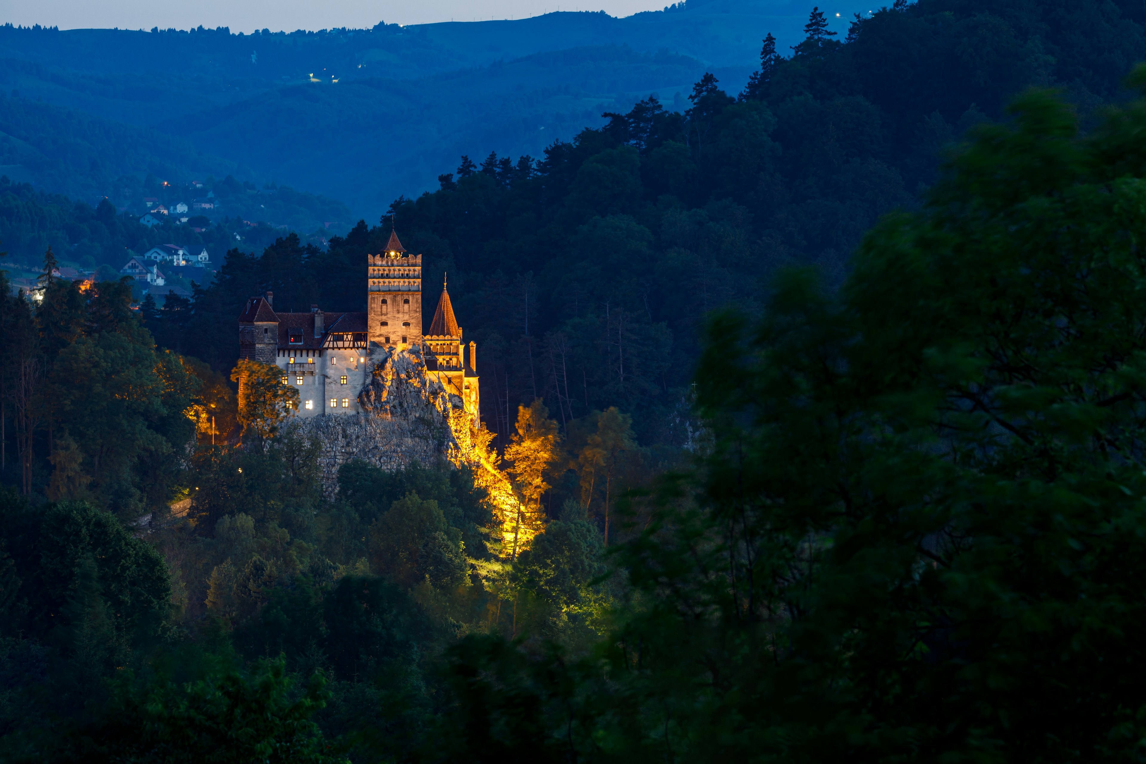 A view of a castle on a cliff top illuminated by night among shadowy hillsides