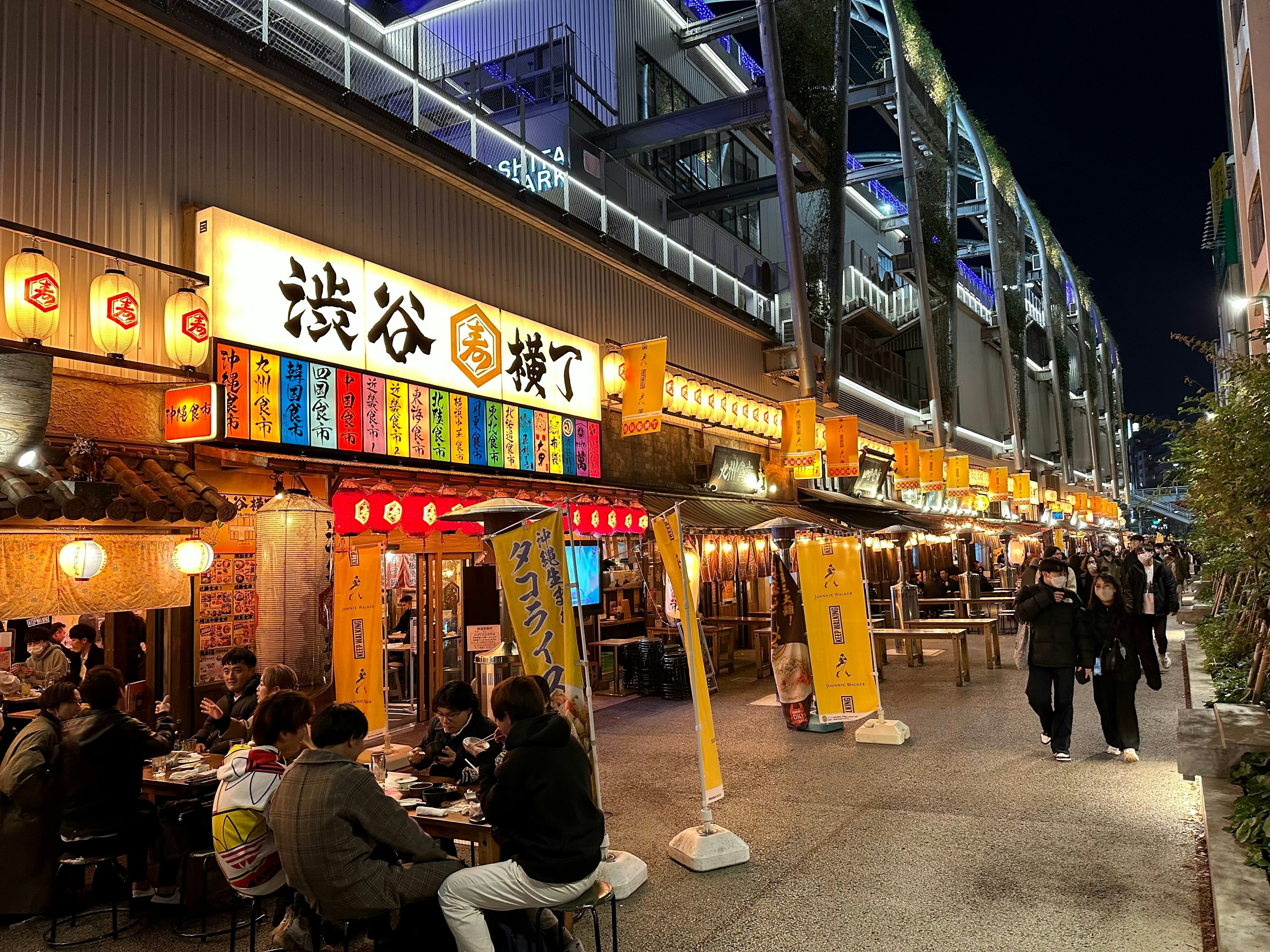 People dine outside a restaurant in an alleyway as people stroll by.