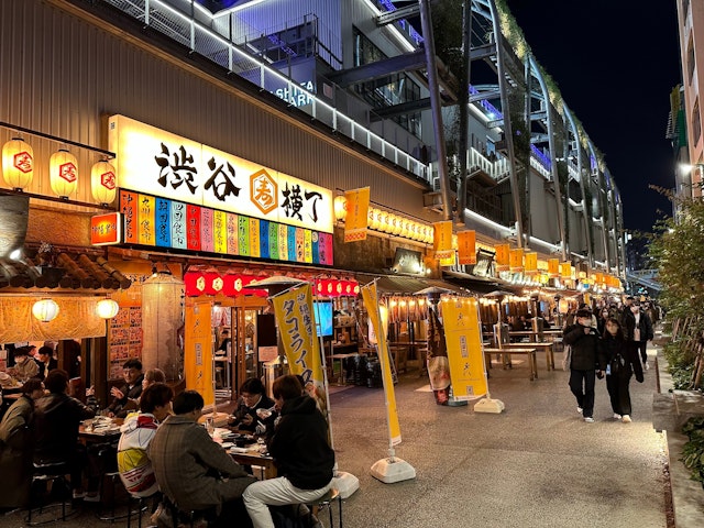 People dine outside a restaurant in an alleyway as people stroll by.