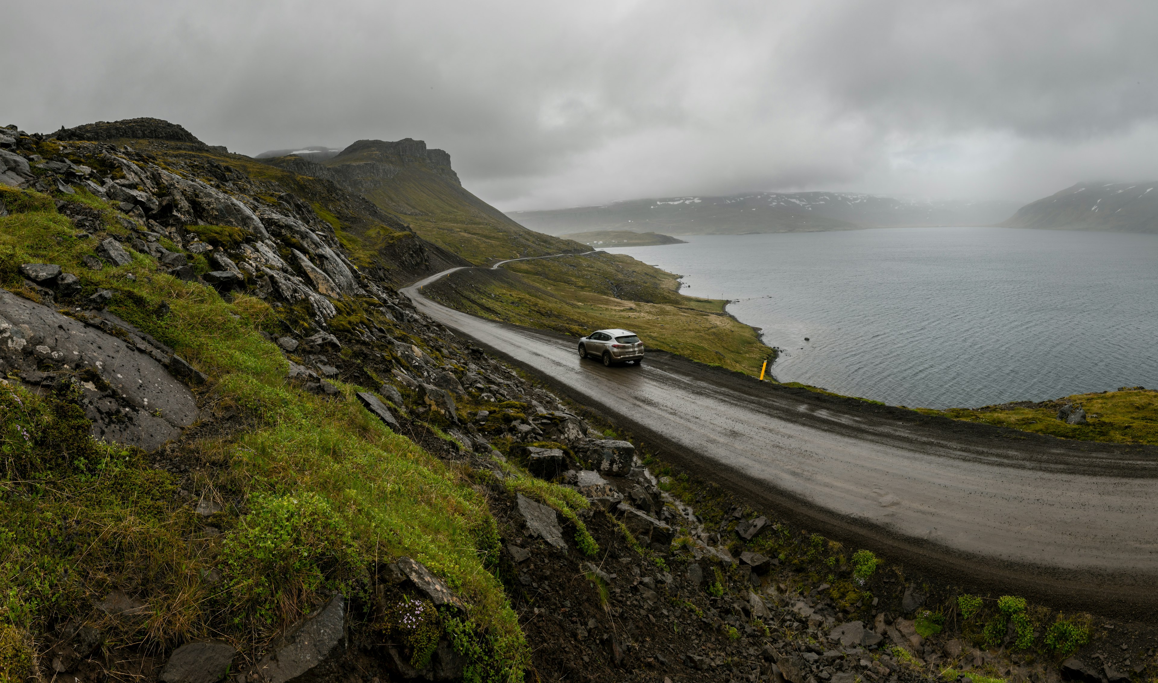 A car driving on a rough and wet coastal gravel road