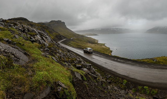 A car driving on a rough and wet coastal gravel road
