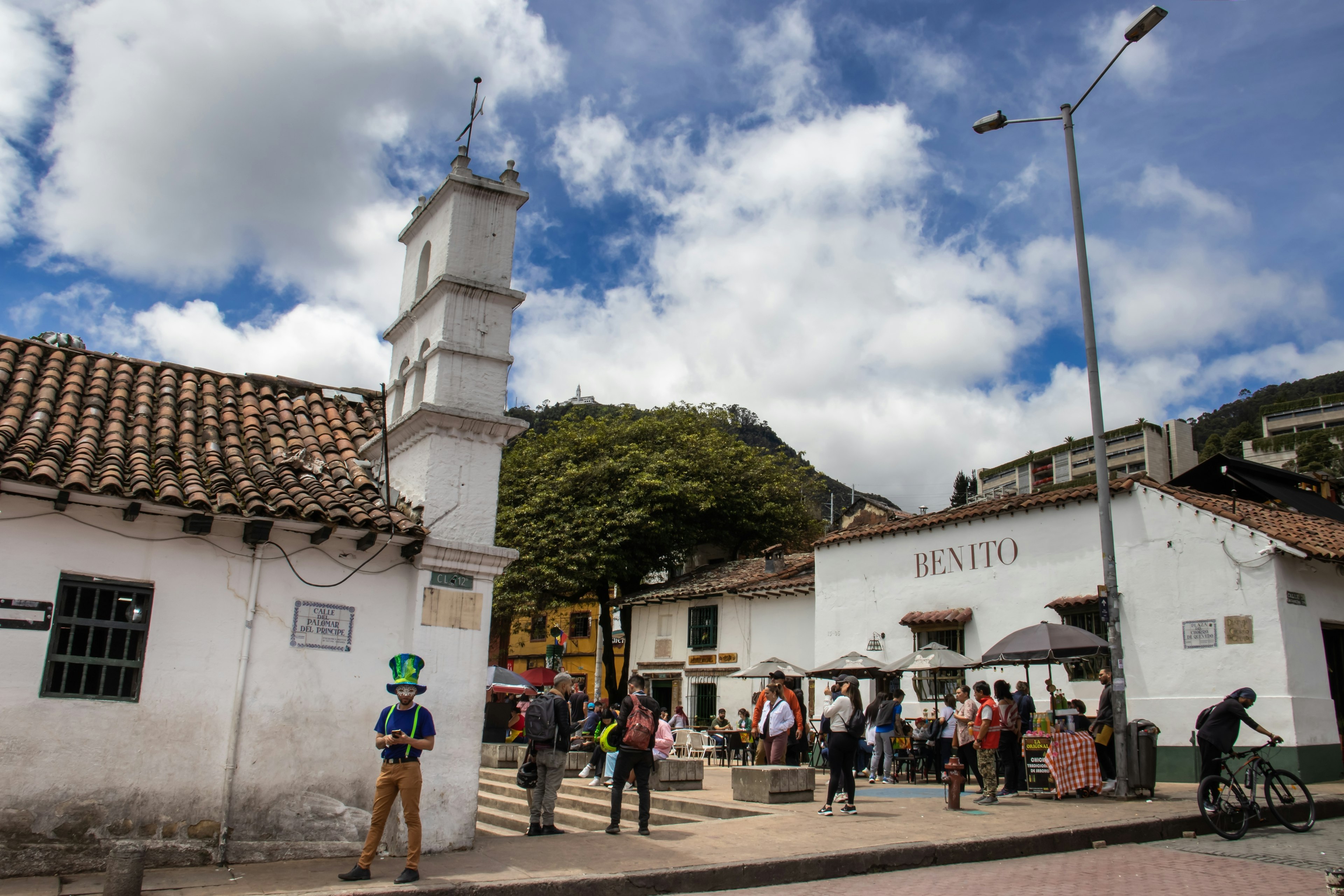 Tourists gather in a plaza with a small church and white-washed buildings