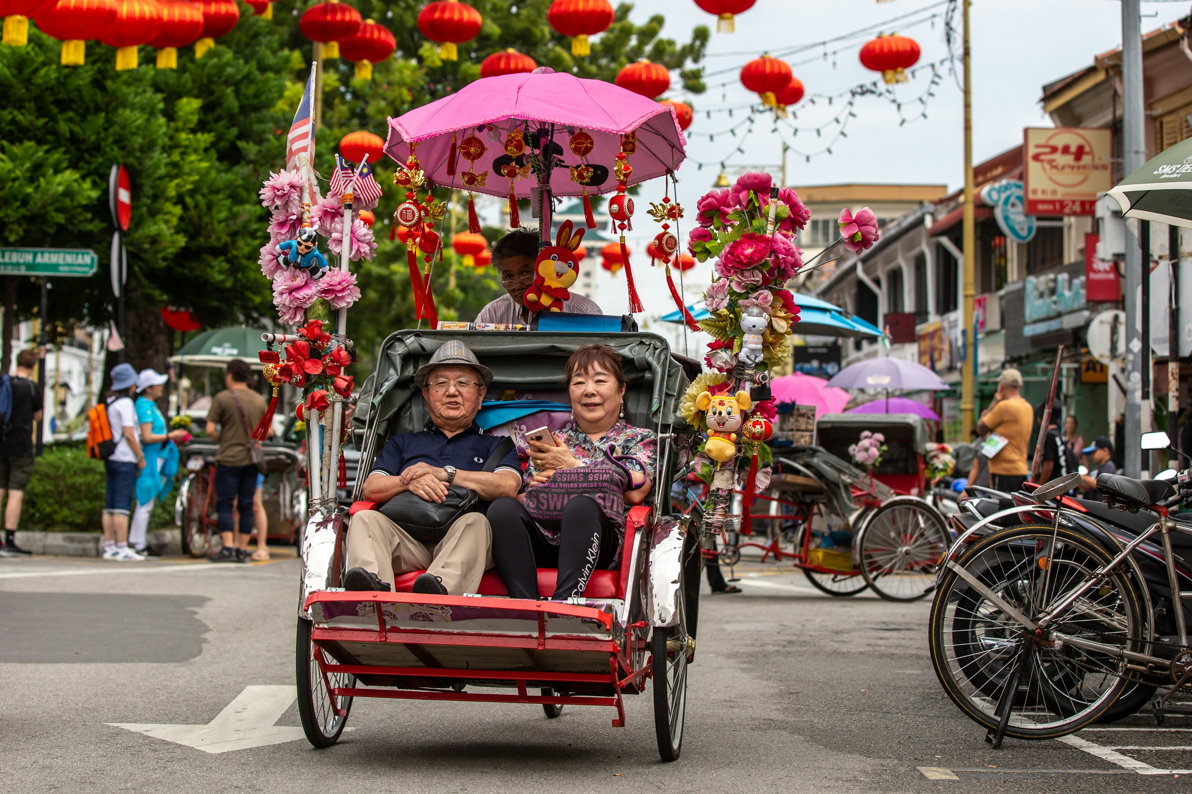 Unidentified people getting pedaled on a trishaw bicycle taxi through the busy streets of George Town, Penang, Malaysia