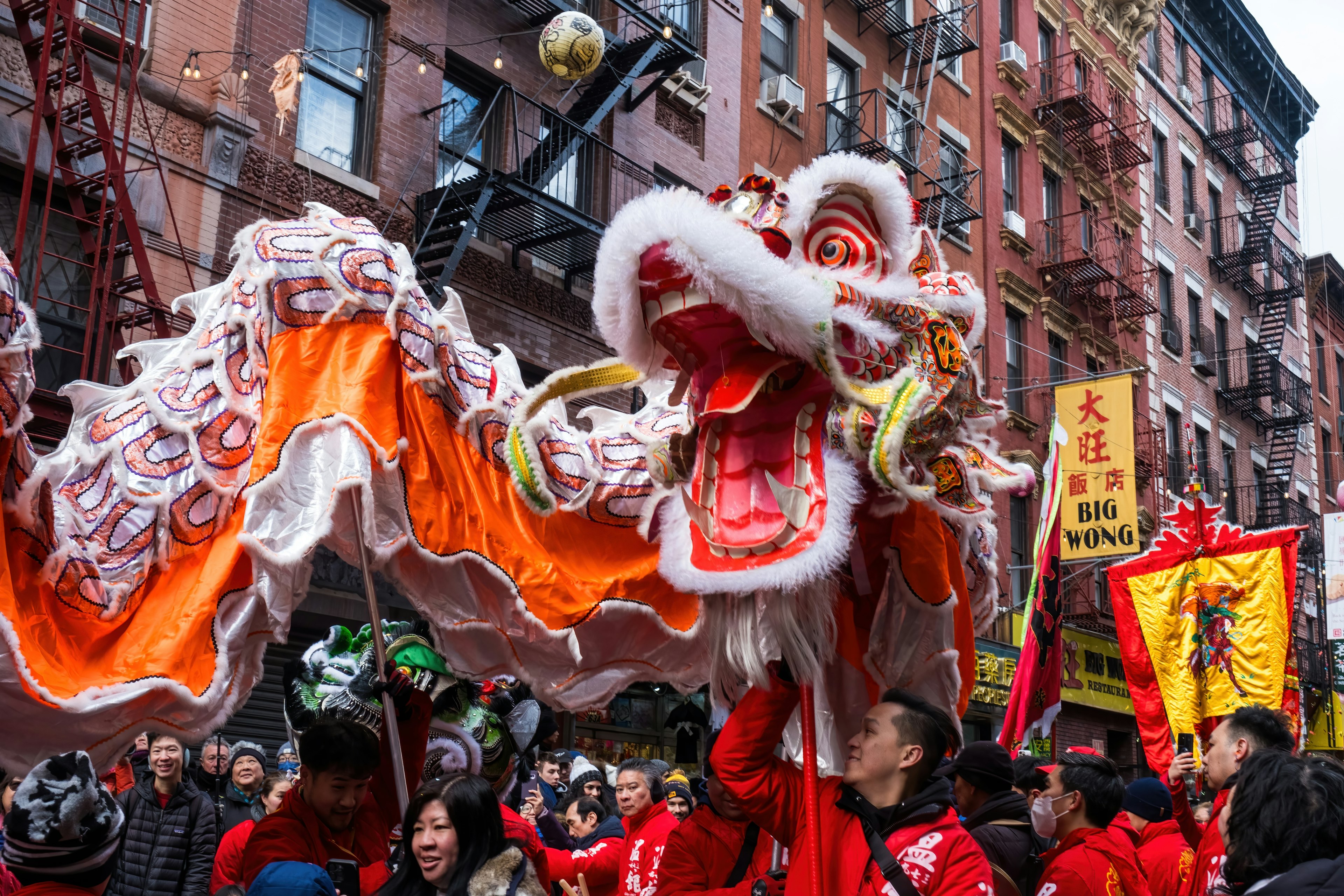 A celebration in the street with a red dragon behing operated by a team of puppeteers