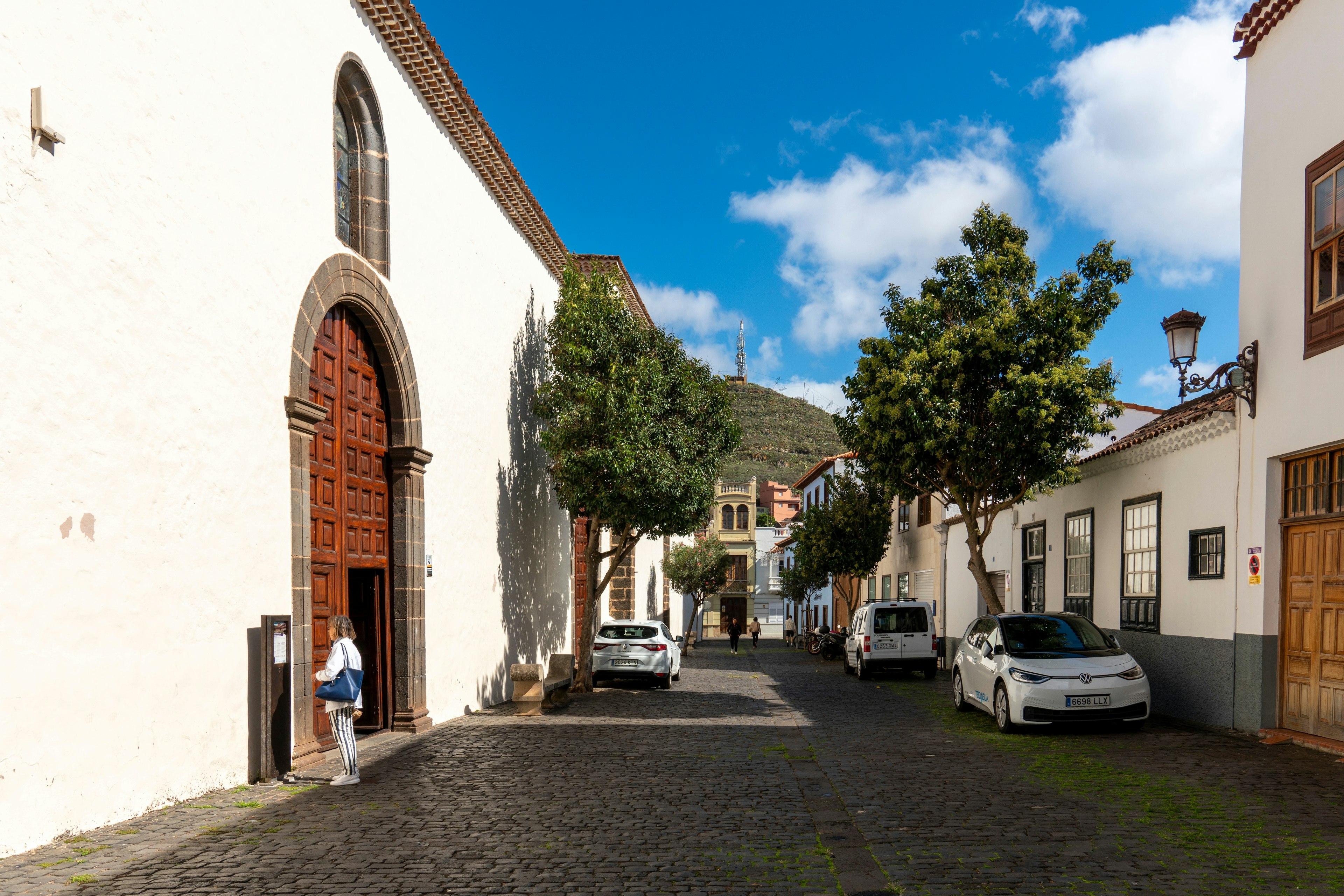 A woman stands in front of an elaborately carved door on a cobbled town streets lined with historic whitewashed buildings