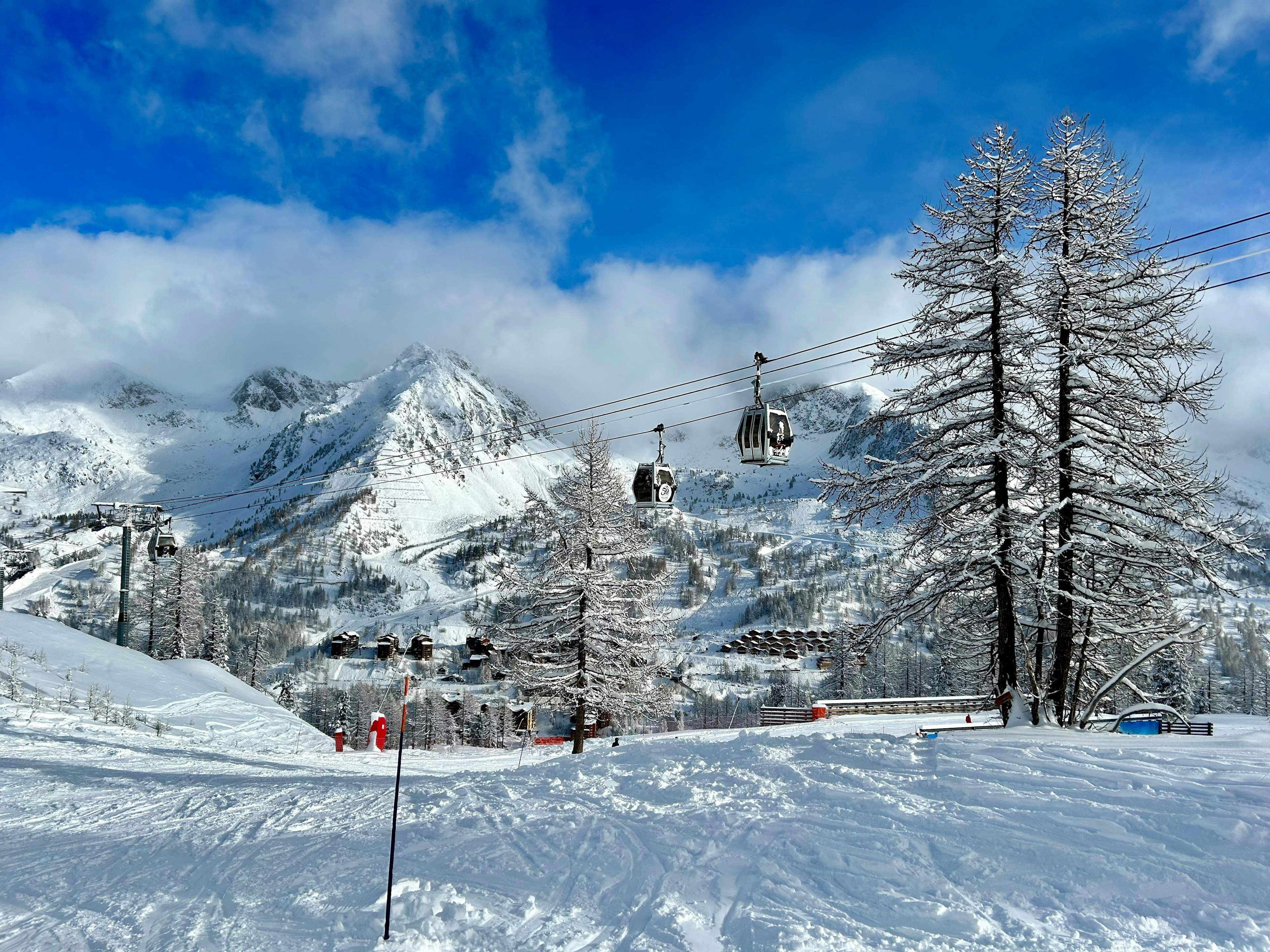 A view of a snowy skiing piste with gondolas ascending and mountain peaks in the distance