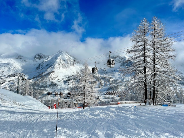 A view of a snowy skiing piste with gondolas ascending and mountain peaks in the distance