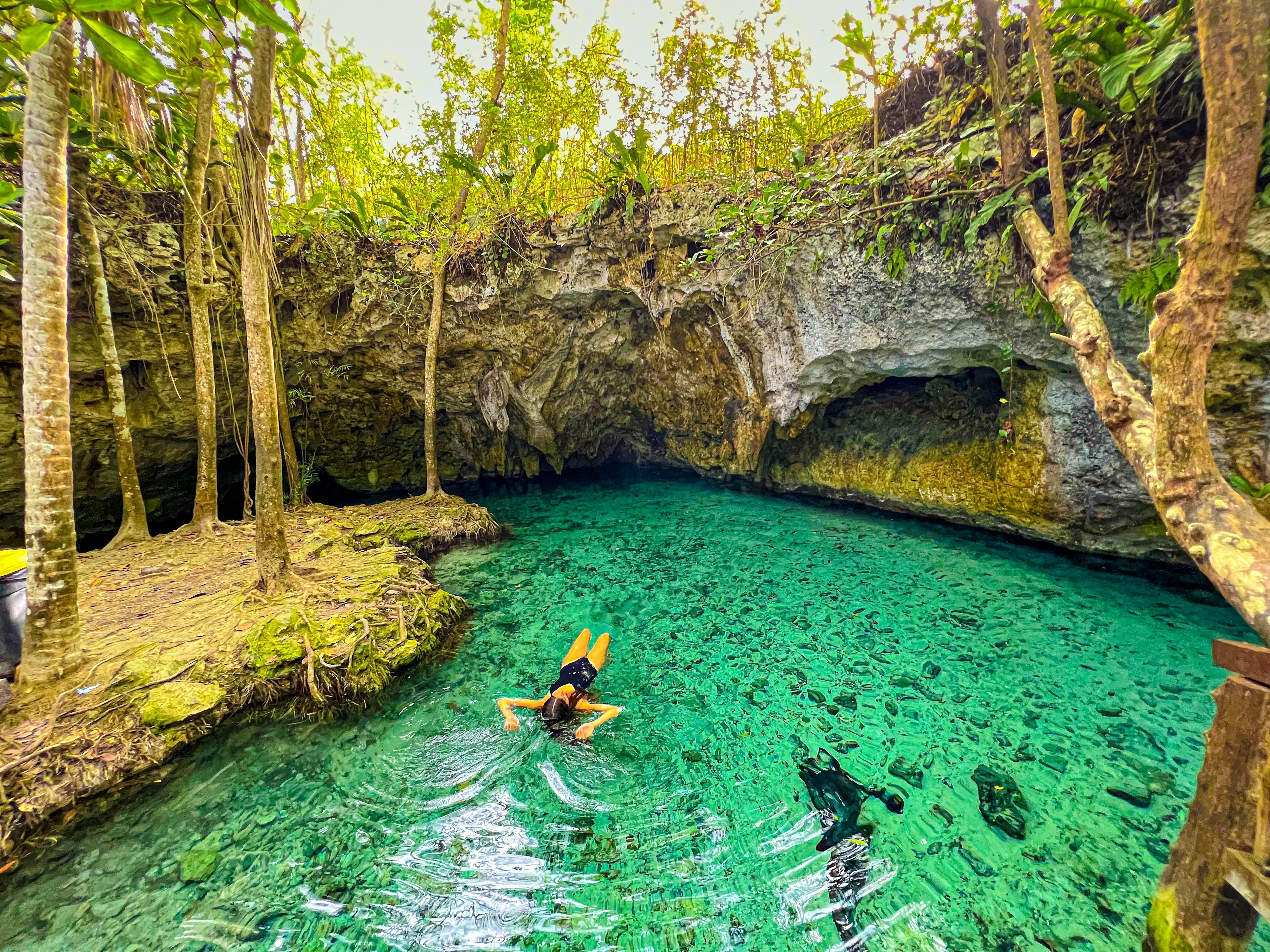 A woman floats on her back in the turquoise waters of a cenote in Tulum.