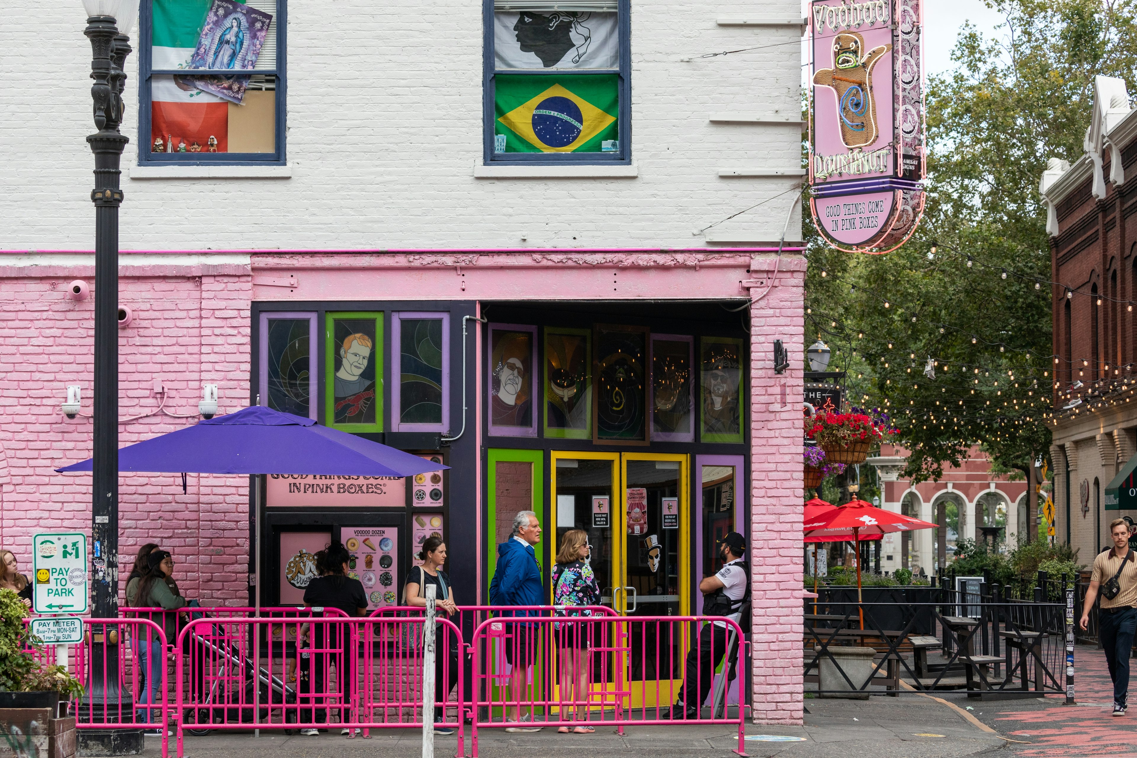 People are waiting in line at Portland's famous tourist attraction, Voodoo Doughnut in Old Town Portland, Oregon. The exterior of the shop is painted pink and there are pink barricades to control the crowd.