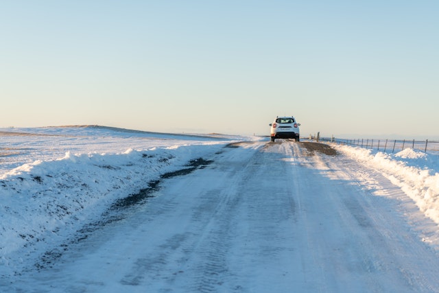 A rear view of a white Dacia Duster driving on a road covered with packed snow and ice through a snowy landscape