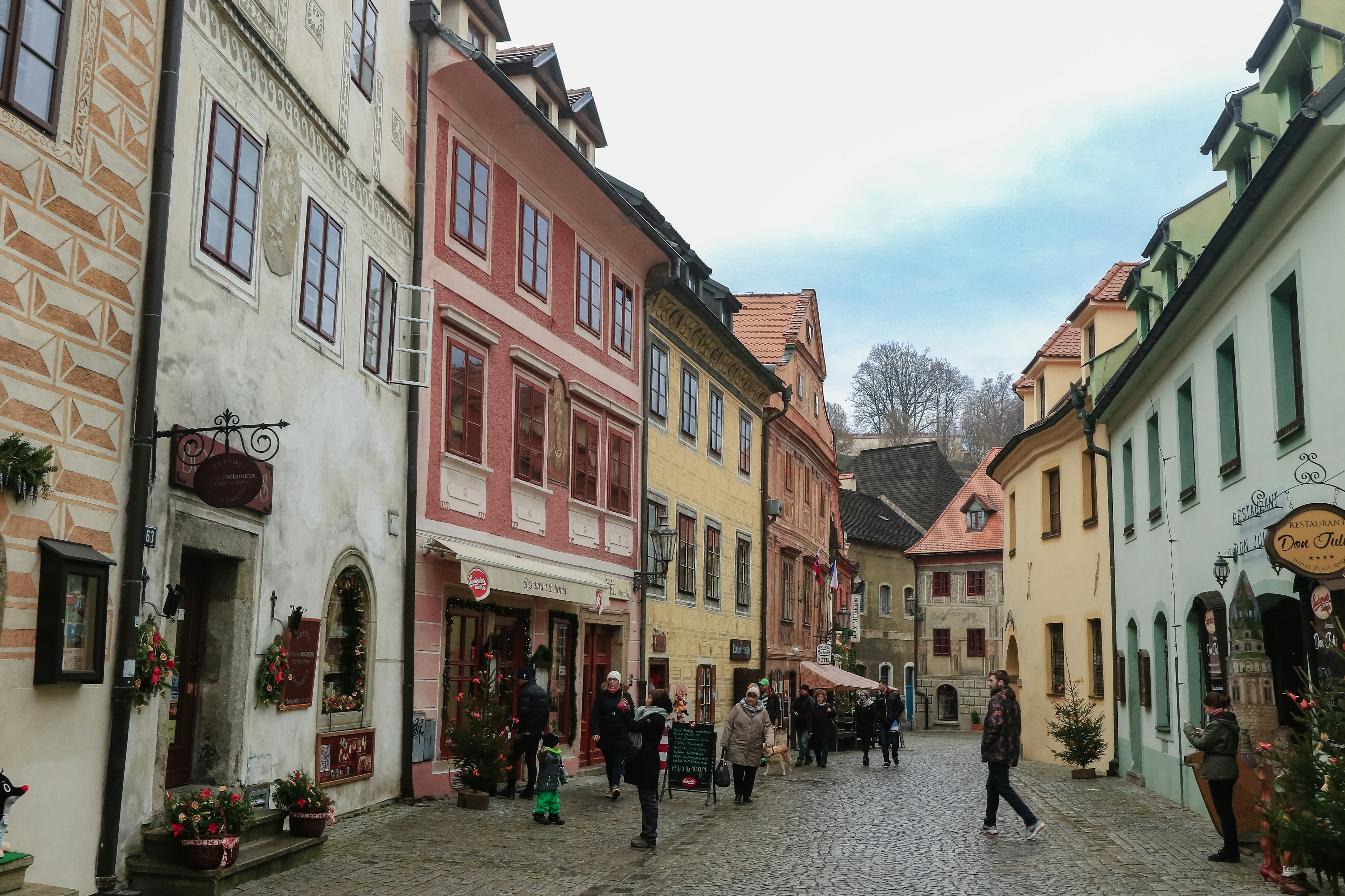 People walk through a narrow street with historic Renaissance houses painted in bright colors on a sunny day