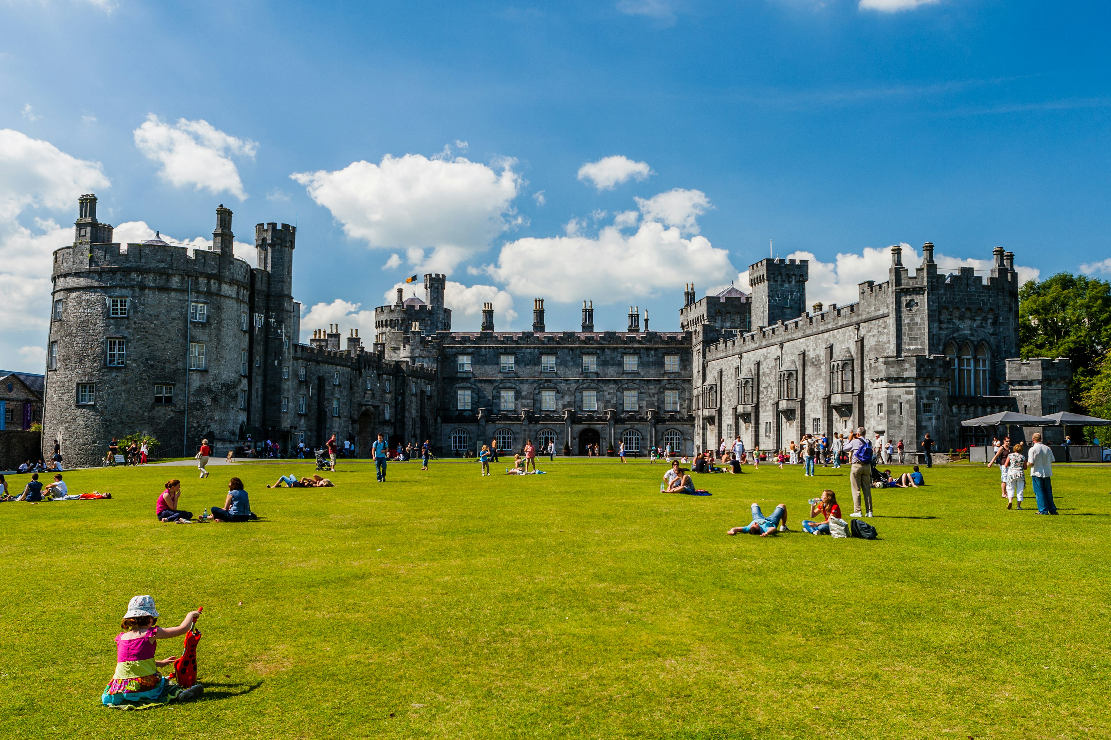 People relax on the lawns outside a vast castle on a sunny day