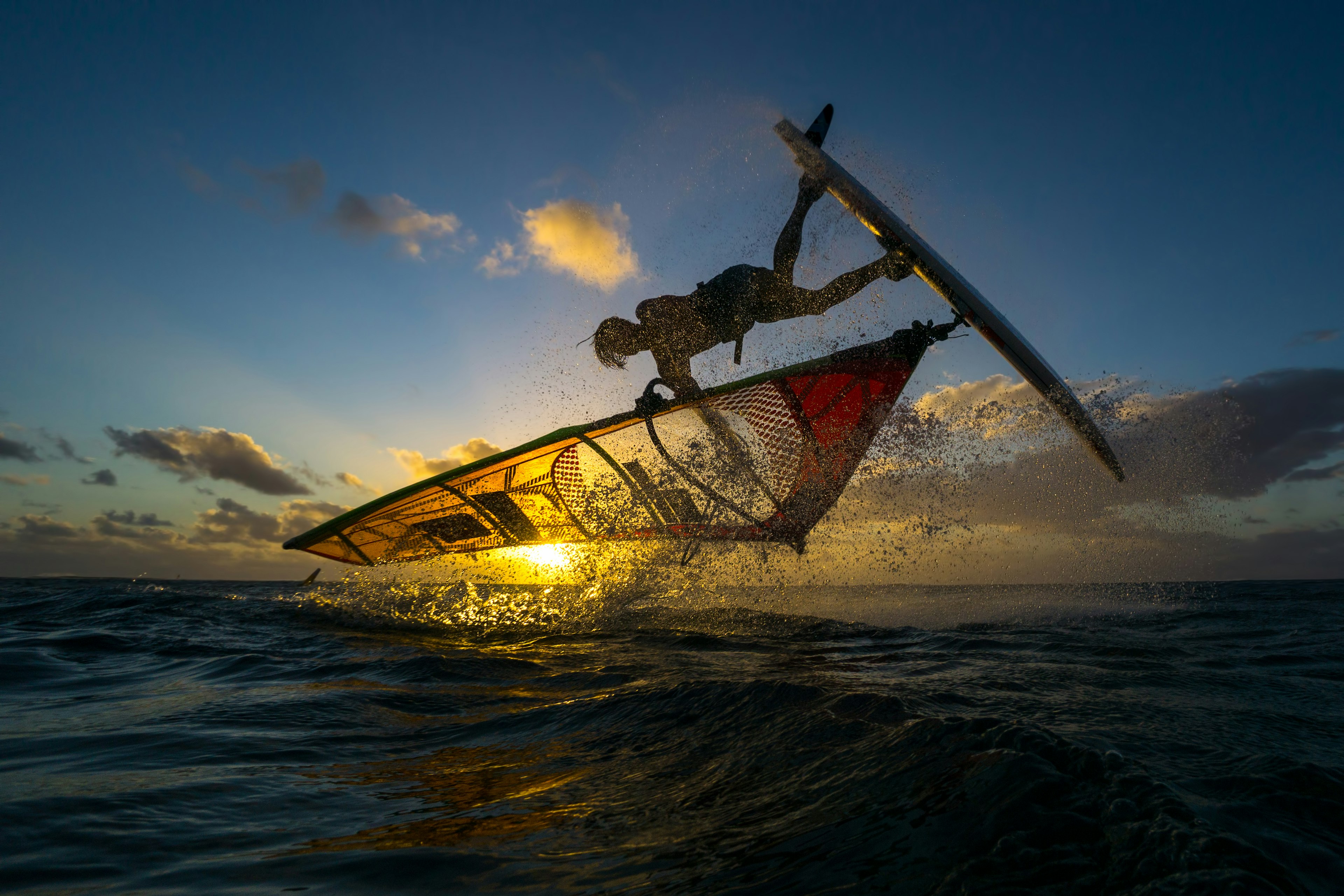 Professional athlete doing incredible trick at windsurfing on the background of a picturesque sunset and spray.