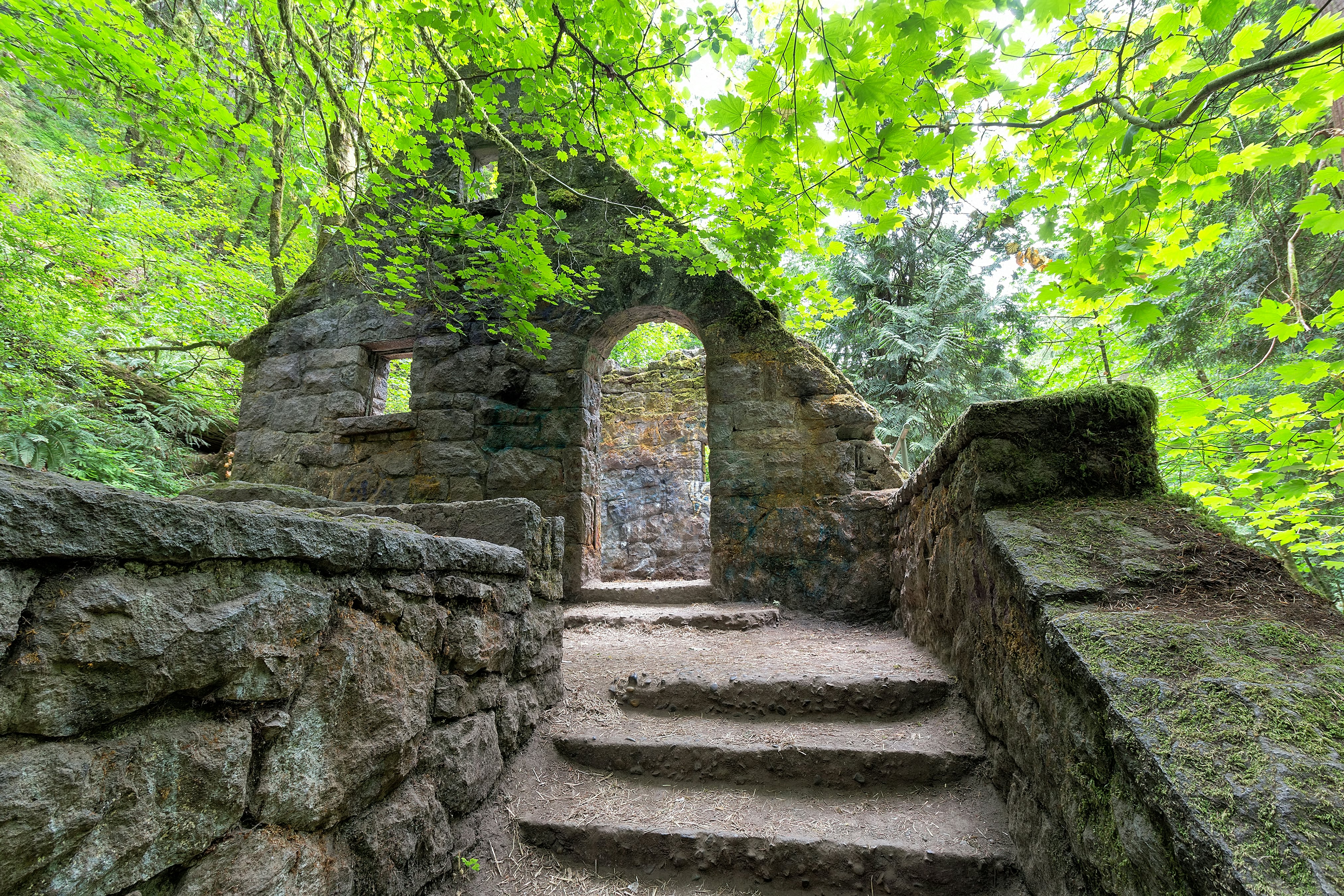 An abandoned stone castle house framed by maple trees at Wildwood Trail in Forest Park, Portland, Oregon, USA