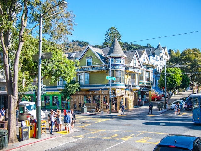 Crowds walk by Victorian-style buildings in the Haight-Ashbury neighborhood in San Francisco, California, USA