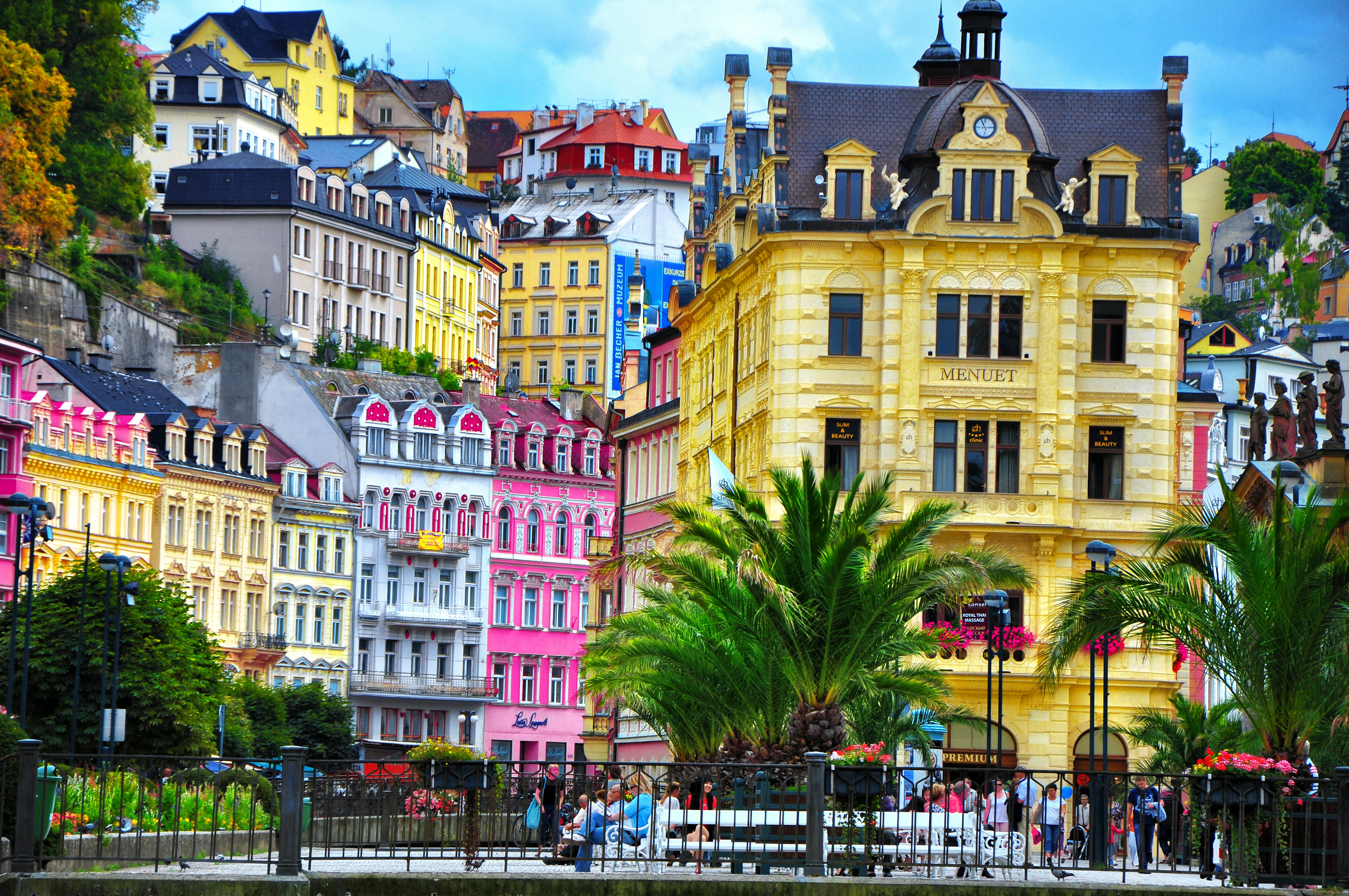 Elegant, brightly painted buildings line a square fringed with palm trees in Karlovy Vary, Czechia