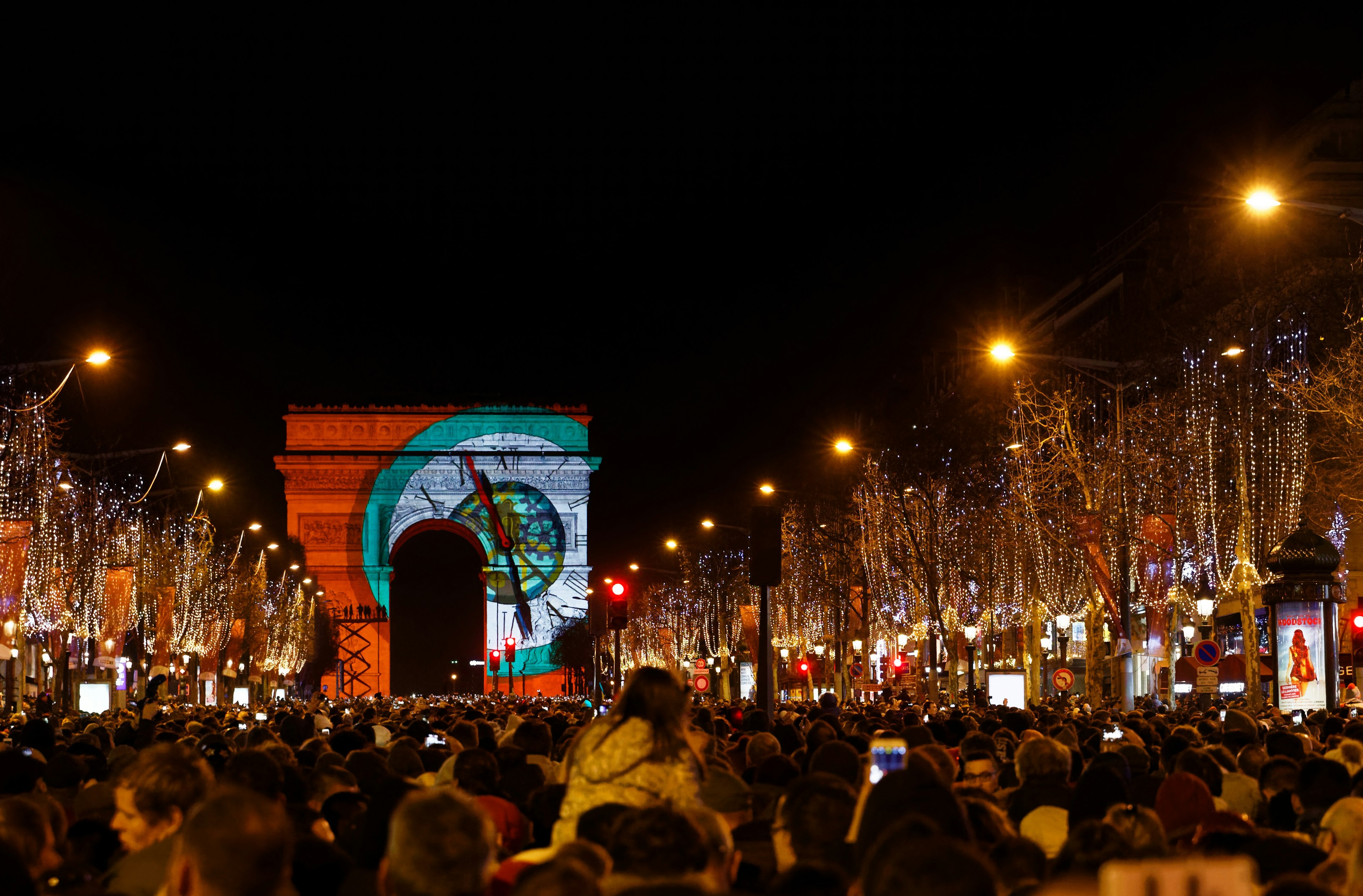 People stand in a crowd facing a large archway with a countdown clock light projected on it.