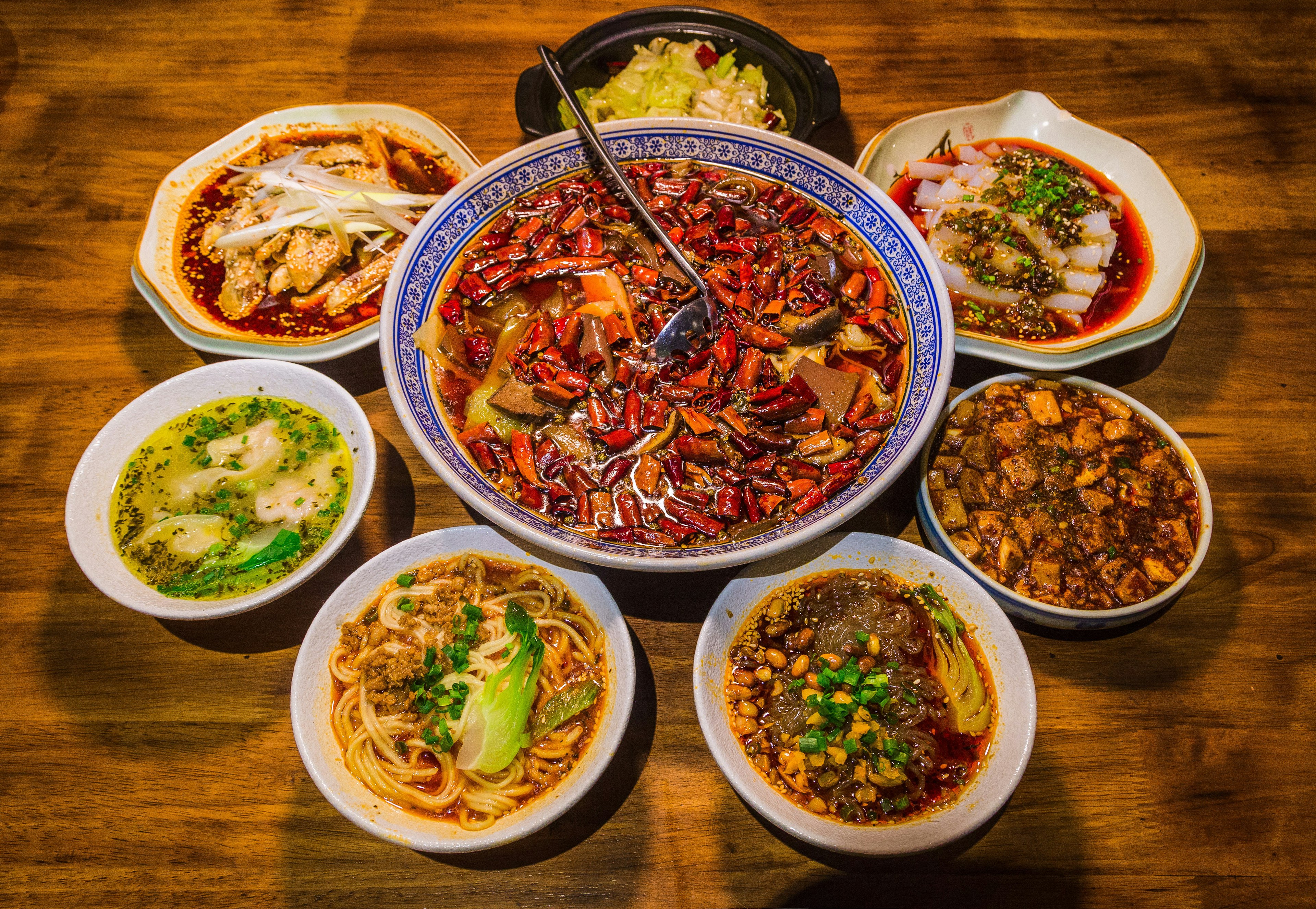 Bowls of different Sichuan foods, including a bowl of red chilli peppers in the middle, and some bowls of noodles.