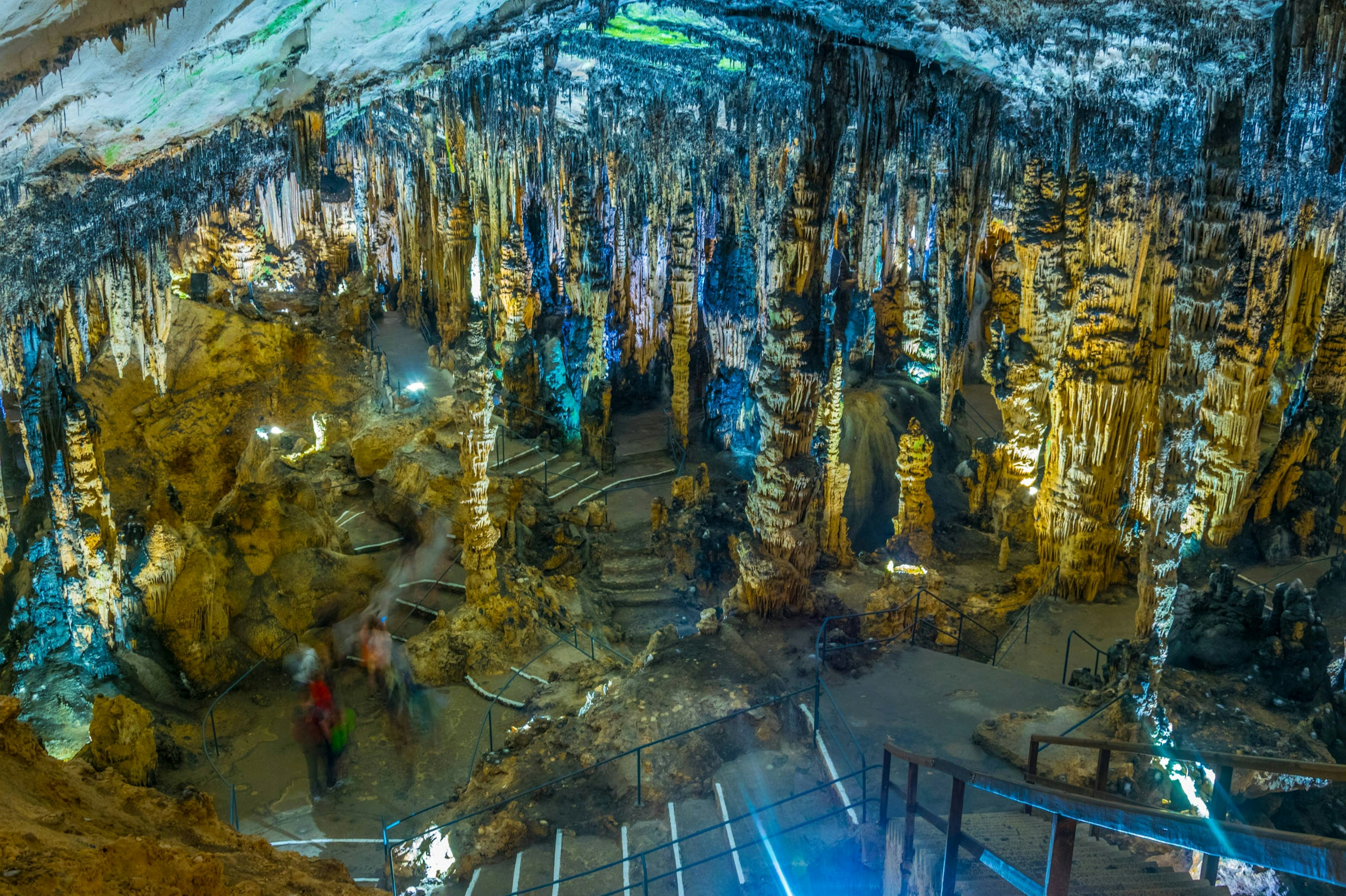 Looking down at a group of people in one of the limestone caves at Coves d’Artà, full of golden stalagmites.