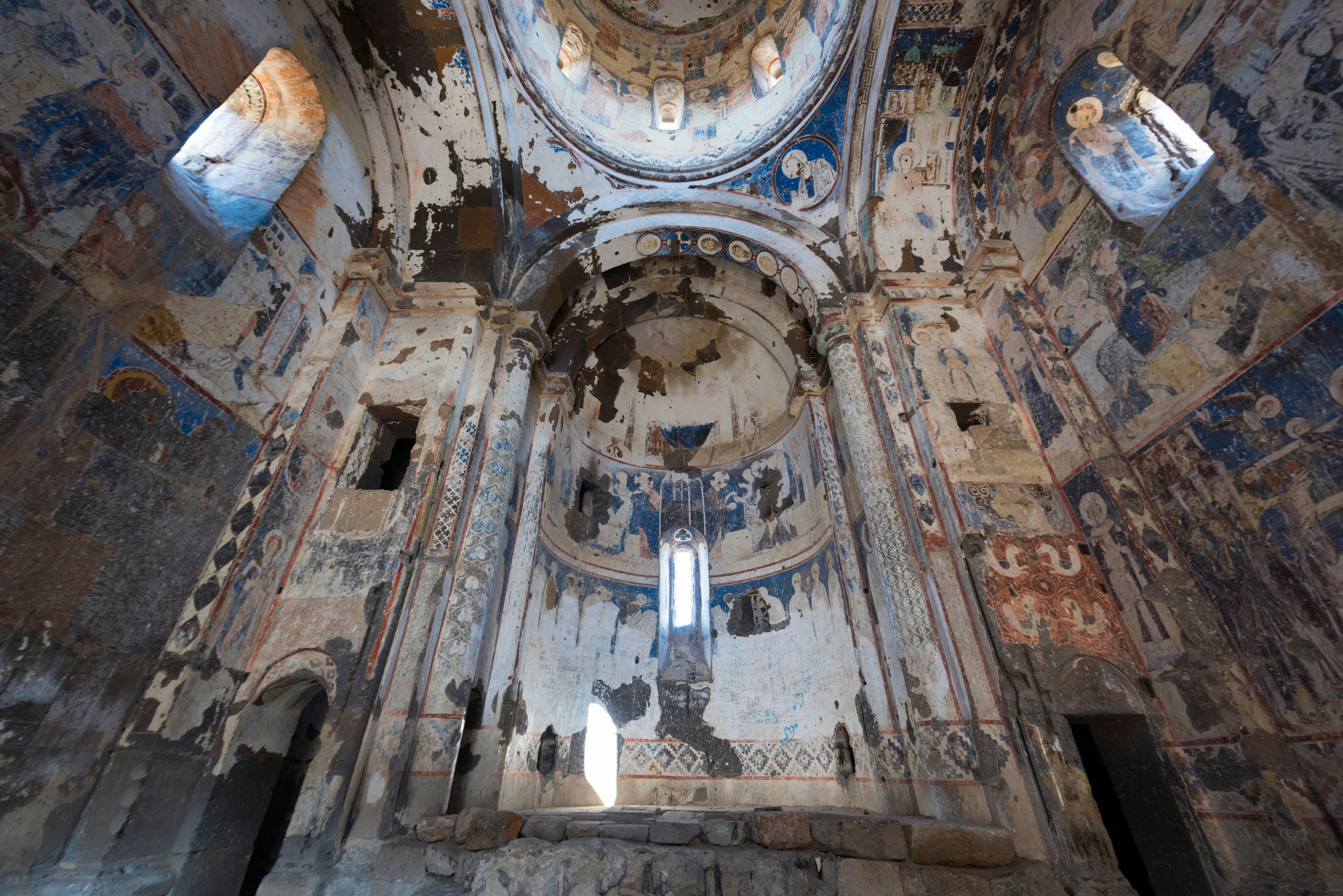 Colourful but faded and time-worn frescoes inside a domed church.