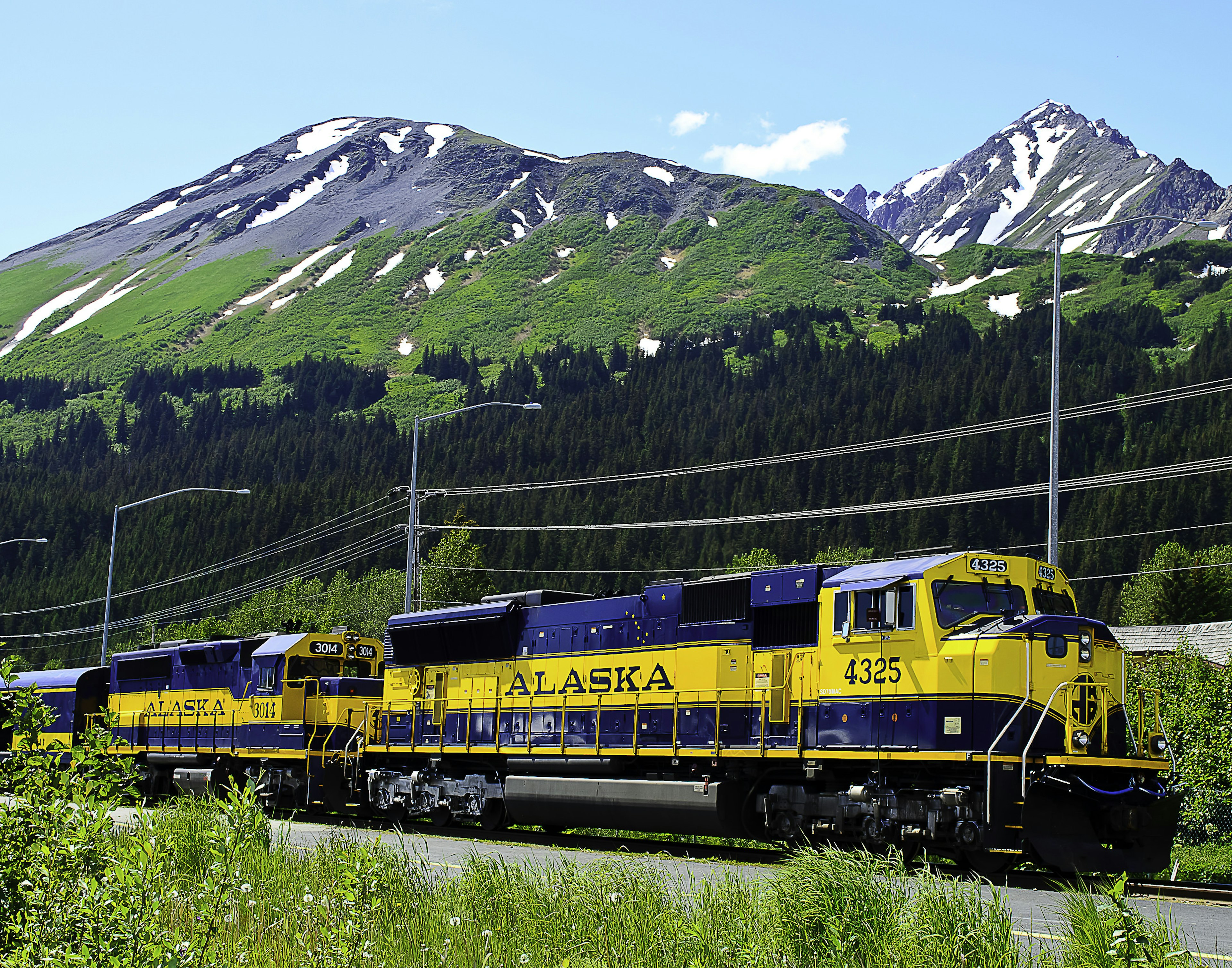 A sturdy navy and yellow train, standing on a platform. On the side of the front car, 'Alaska' is written in yellow letters