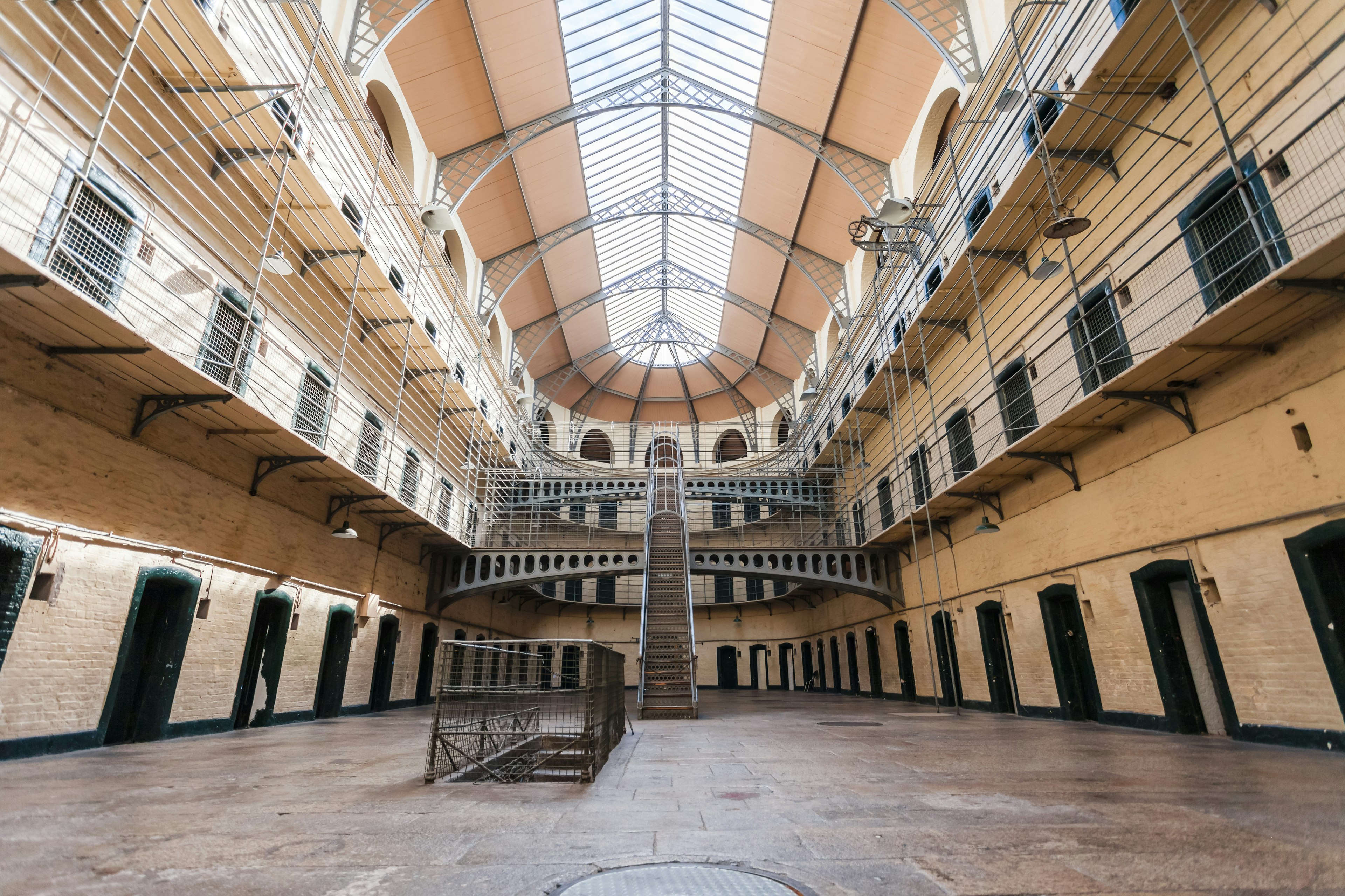 Interior of a Victorian prison with many cell doors and a staircase leading up to narrow walkways