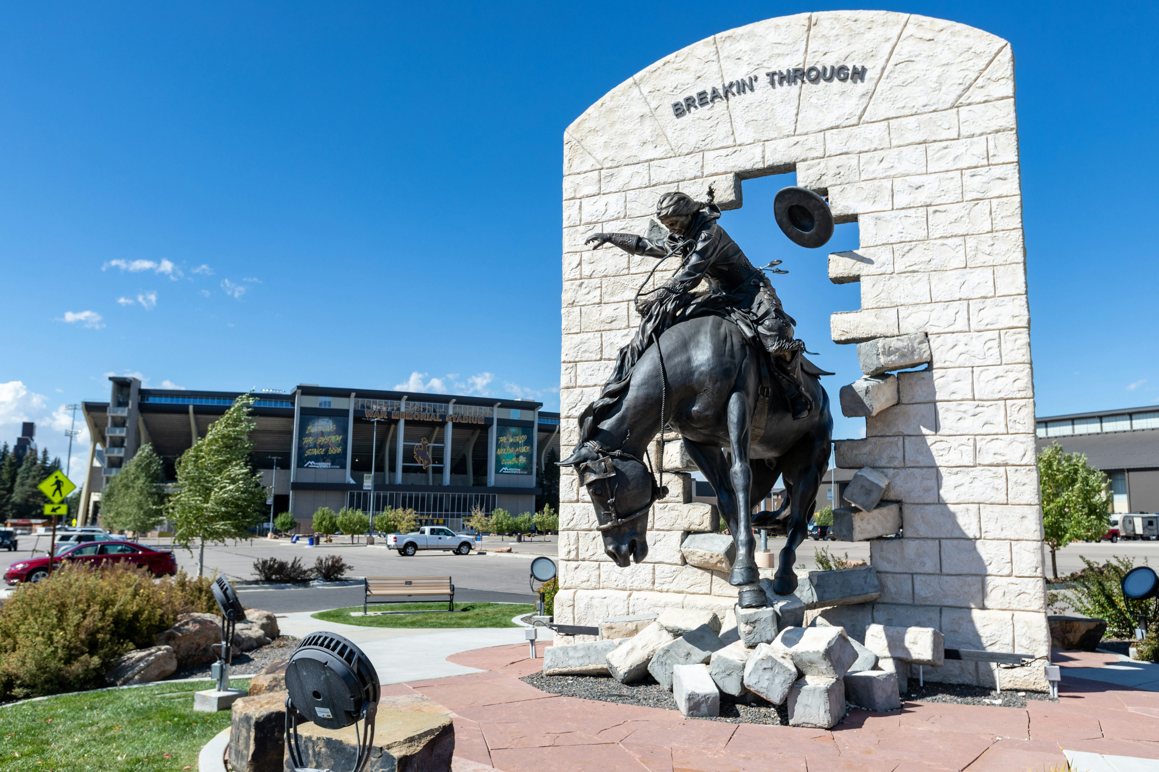 A statue of a man riding a bucking horse stands in front of a stadium.