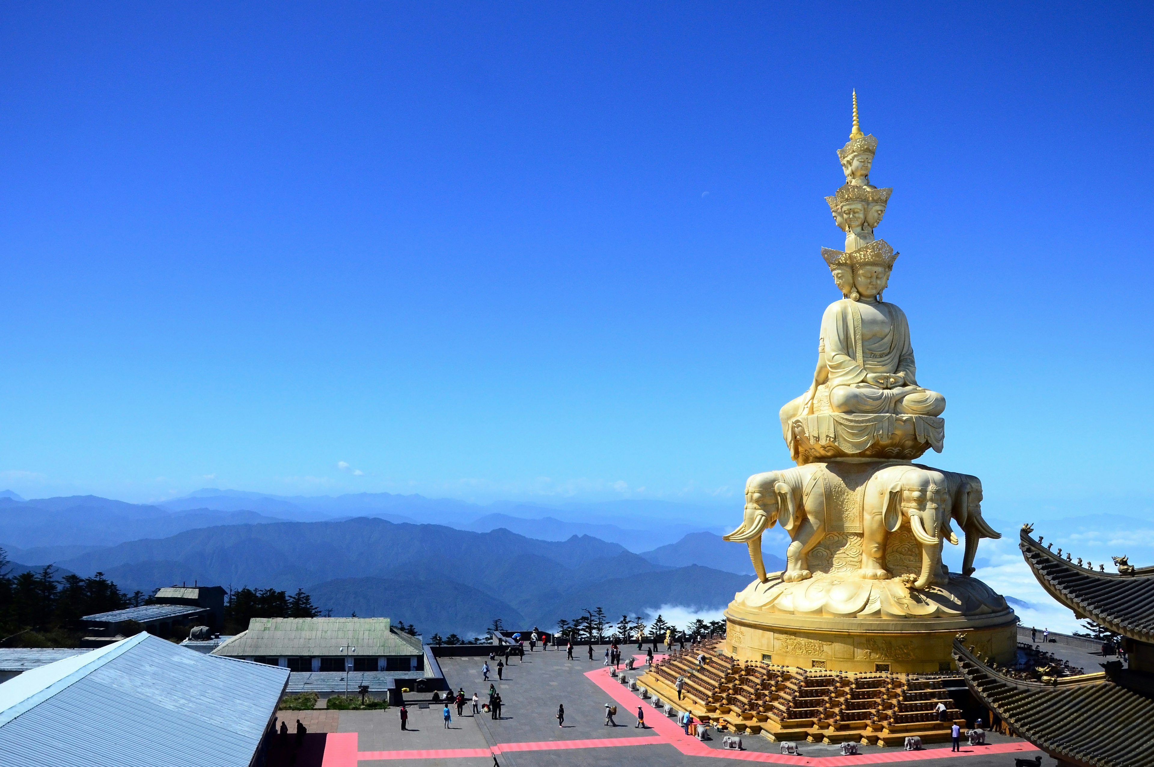 A large golden Buddha statue stands atop a mountain overlooking mountains covered in clouds and mist.