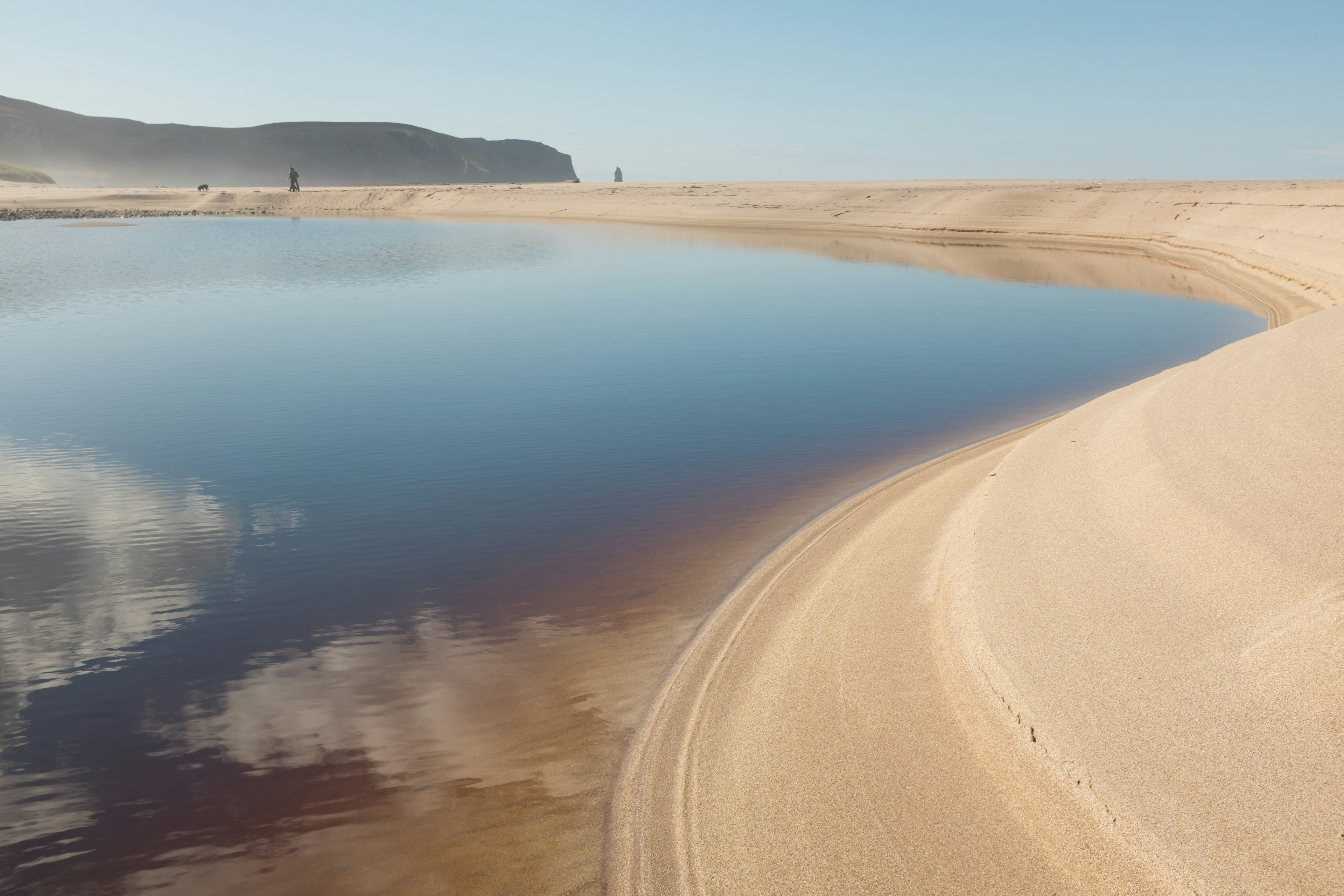 Steep white sand curves around the fresh water lagoon at The Sandwood bay beach, Sutherland, Scotland, UK.