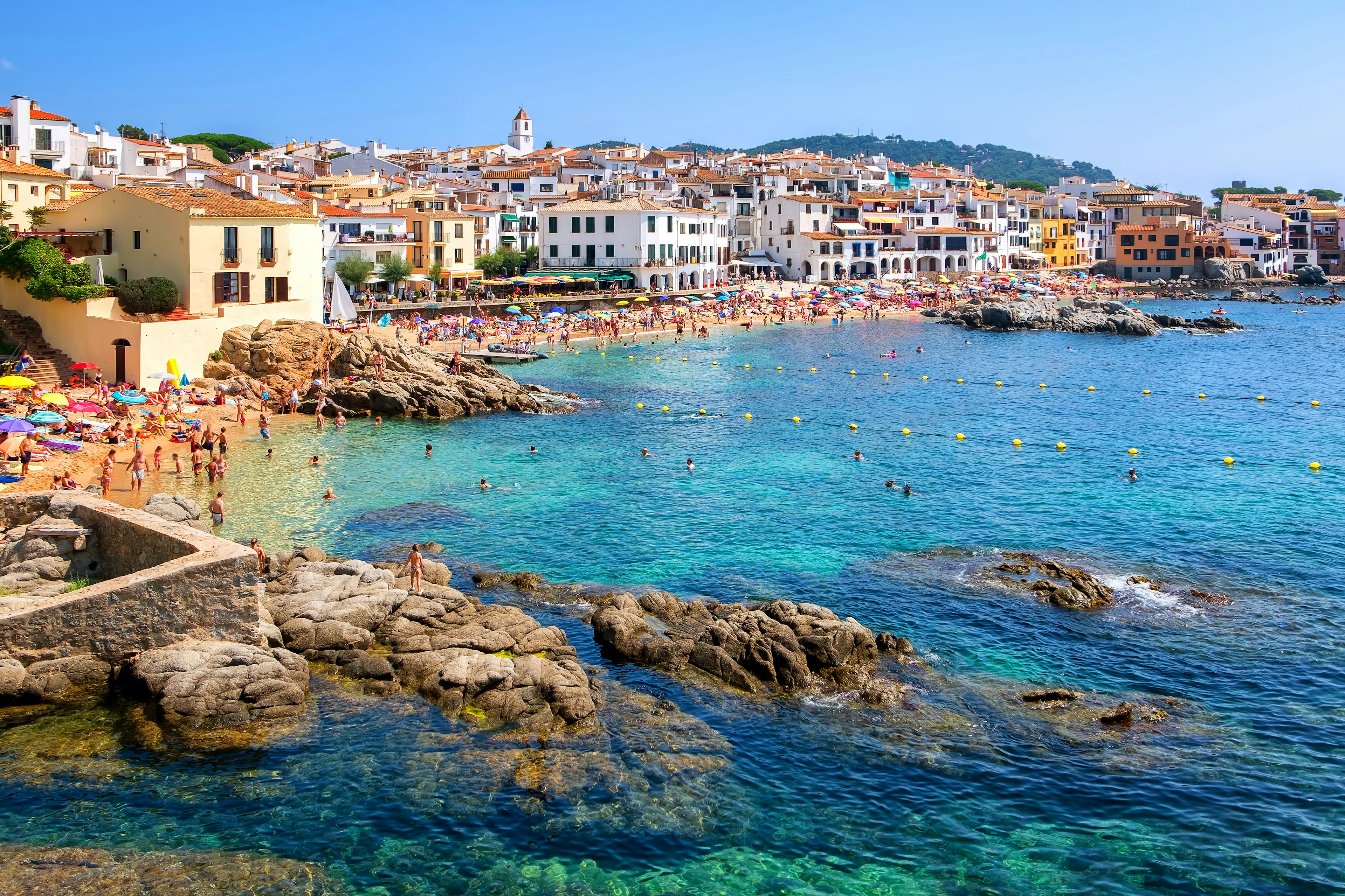 A traditional whitewashed fishing village with a beach packed with people on a sunny day