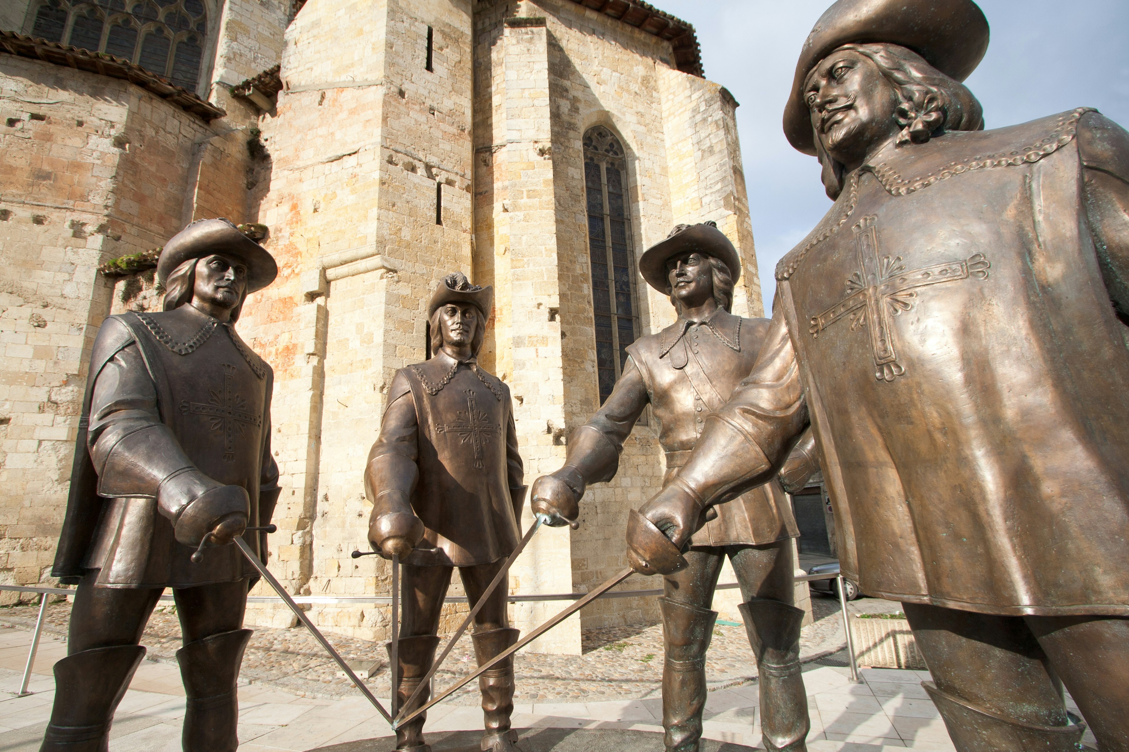 Statues of the musketeers stand guard outside Condom Cathedral, holding their sword blades together.