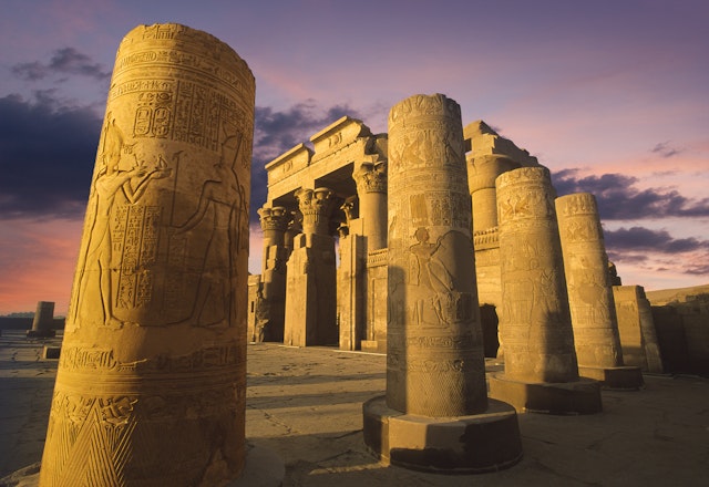 An Egyptian temple with large stone columns covered in etchings and hieroglyphics lit up in the evening as the sun sets